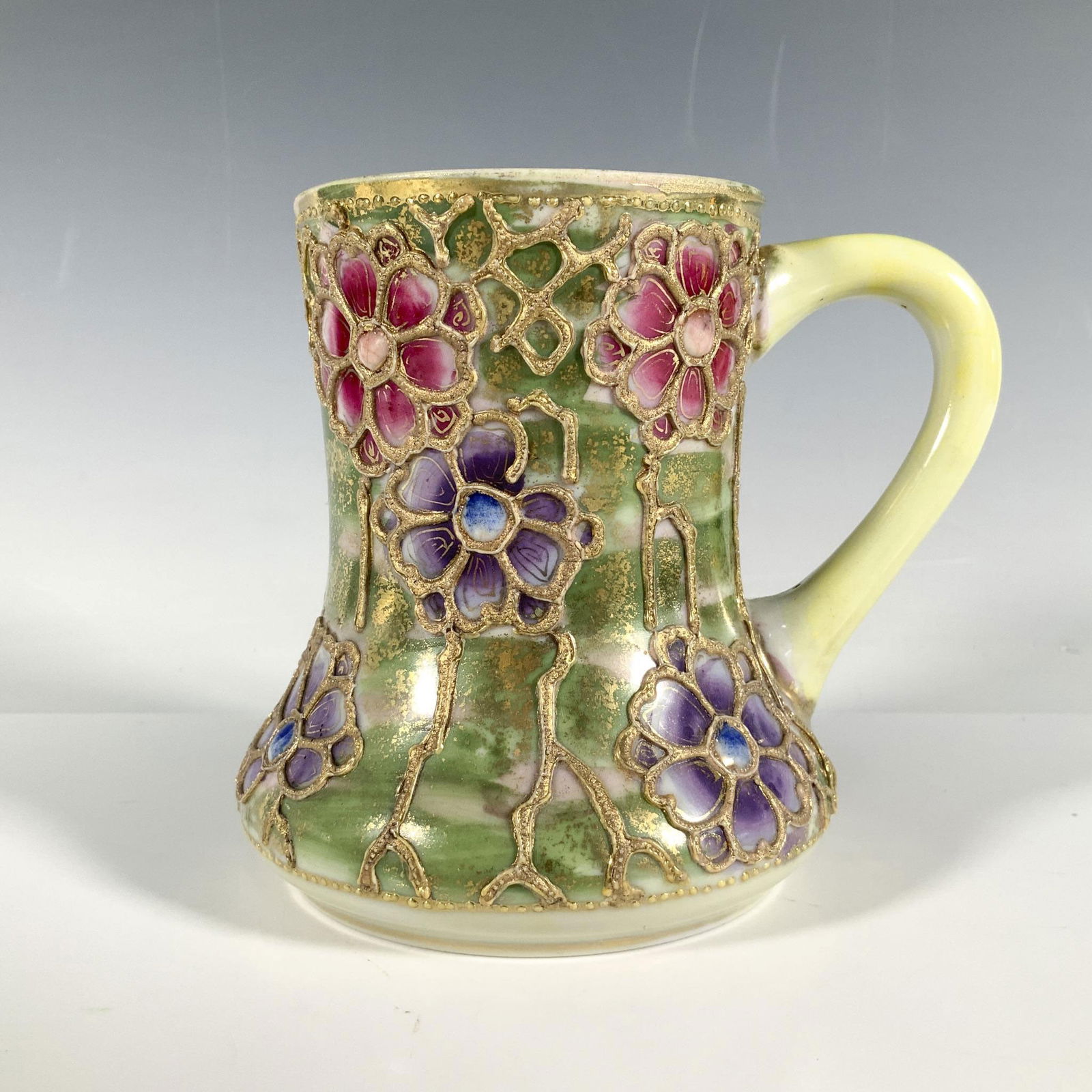 Vintage Gilded Japanese Mug: Gorgeous hand painted mug with raised gilding. Green base color with purple and pink flowers. Nippon backstamp. Dimensions: 5"L x 4.25"W x 4.25"H