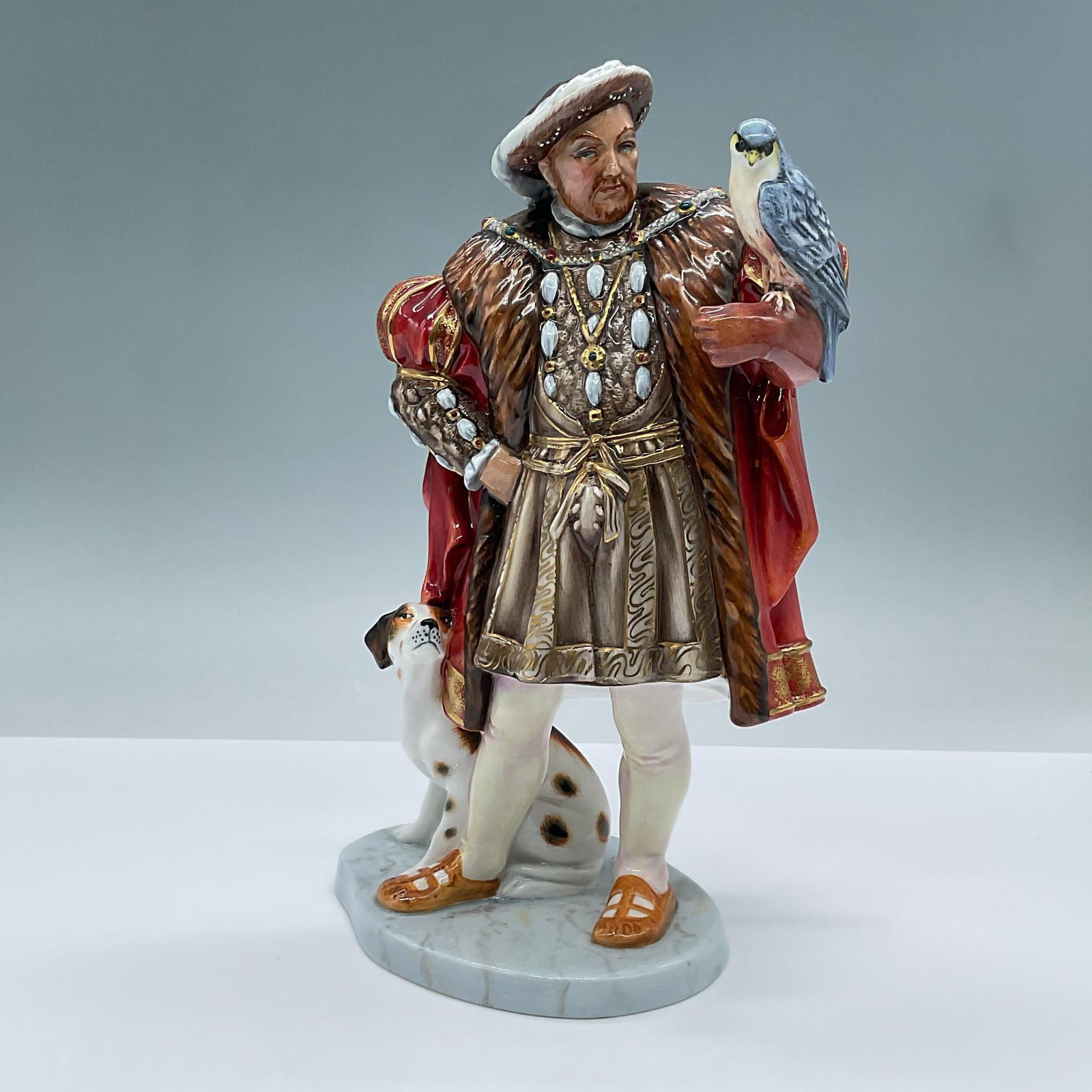 Henry VIII HN3350 - Royal Doulton Figurine: This limited edition figure features a regal King Henry VIII fashioned in opulent 16th century garments with gilded gold accents. A falcon is perched on one arm while a dog sits at the opposite side. 