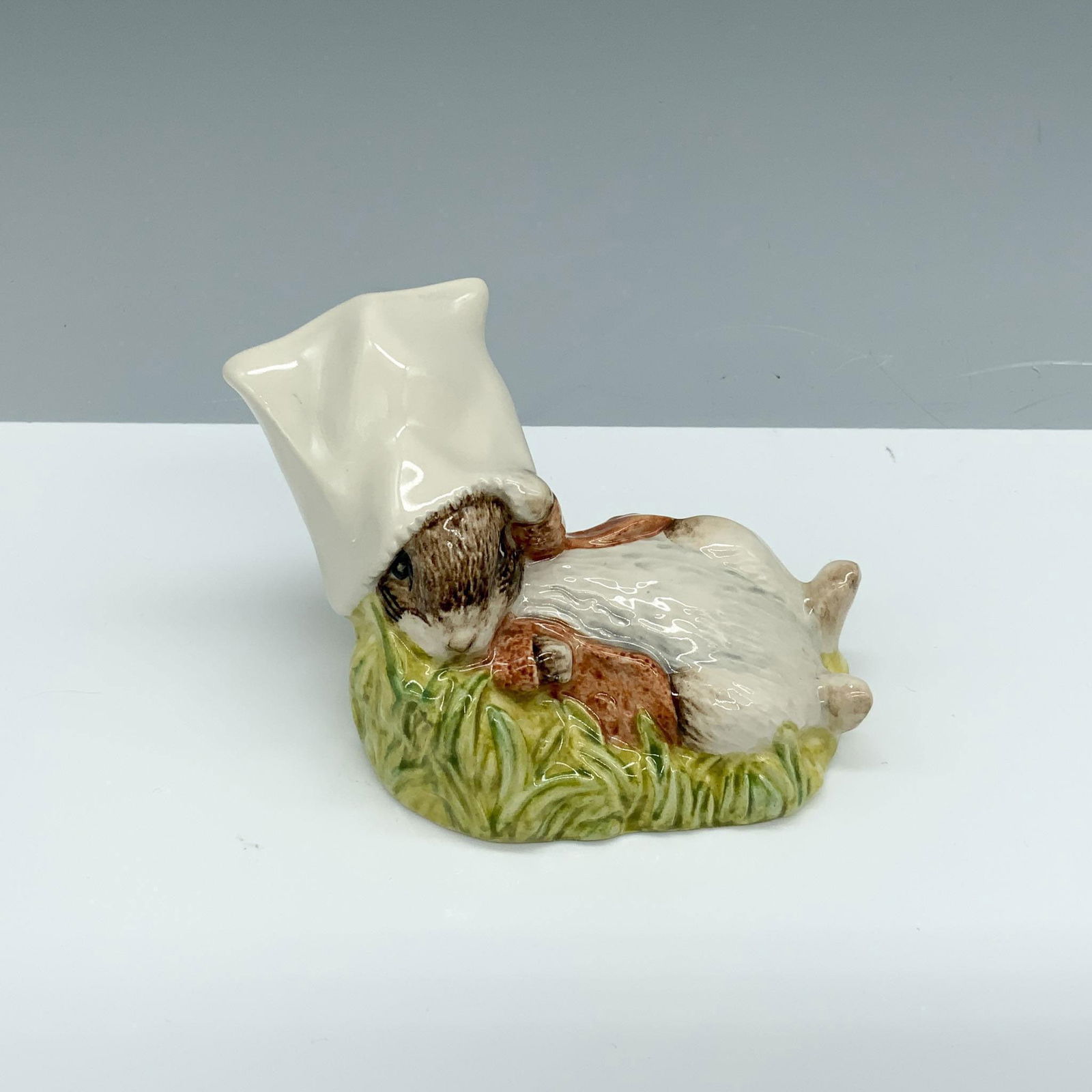 Royal Albert Beatrix Potter Figurine, Benjamin Wakes Up: Glossy porcelain figure of a bunny laying down with a bag on its head. Royal Albert Beatrix Potter backstamp. This item has its original box (3"L x 3"W x 4.25"H). Issued: c. 1990 Dimensions: 3.75"L x