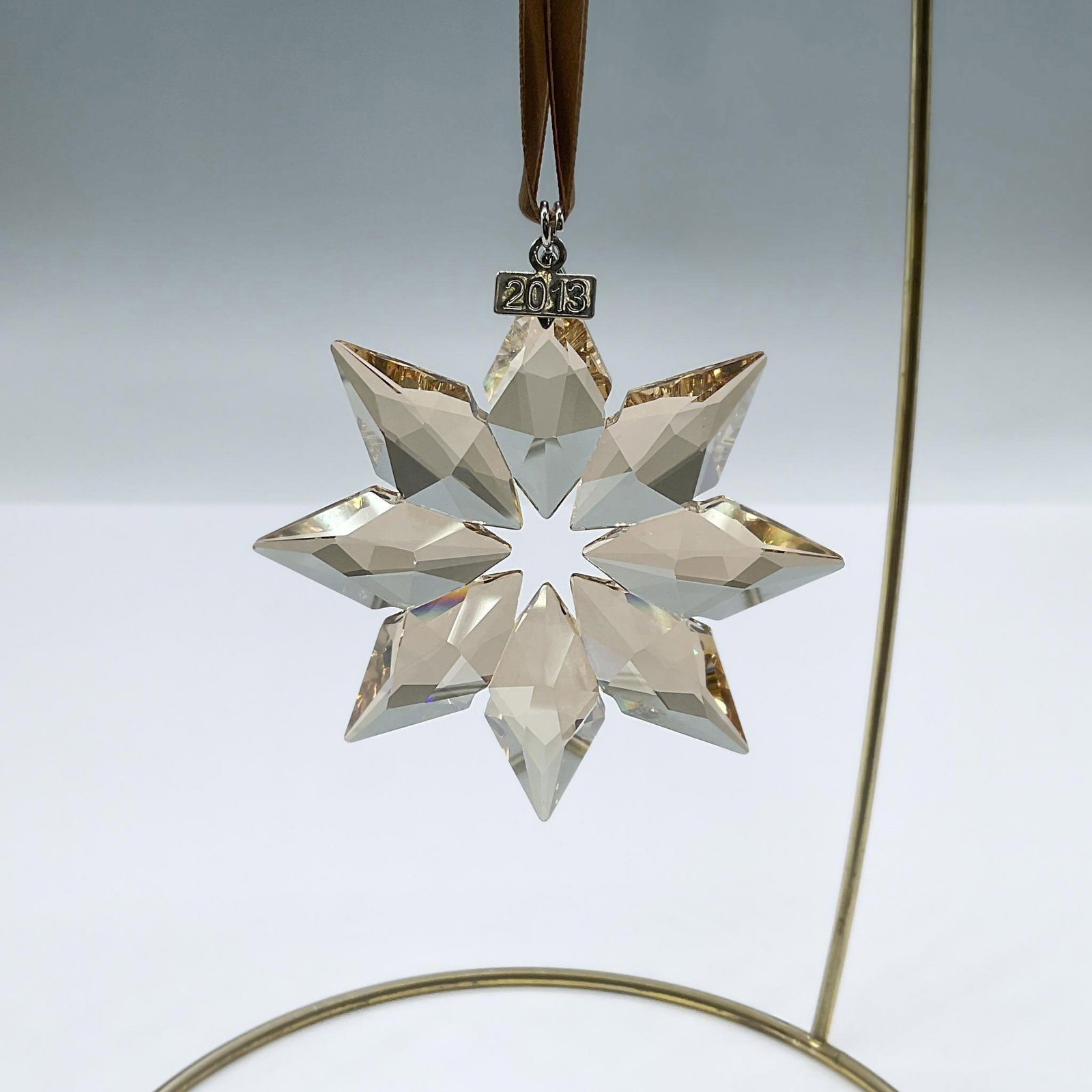 Swarovski Crystal Figurine, SCS Gold Christmas Ornament: This sophisticated star features a crystal golden shadow which reflects light in a unique way. It has a silver tone metal tag and brown satin ribbon. Swarovski engraving. 5004491. Issued: 2013 Dimensi