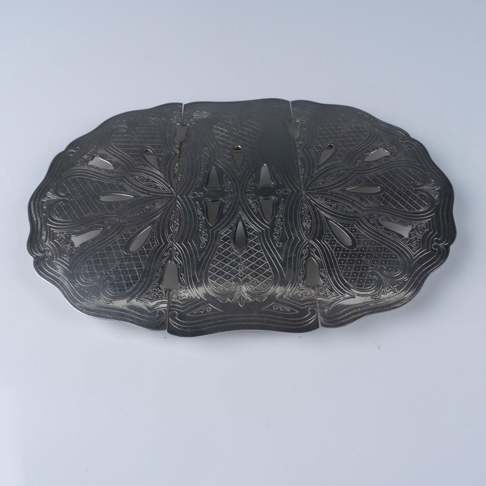 De Uberti Italian Silverplate Expandable Trivet: A finely crafted silverplate expandable trivet by De Uberti, Italy. This elegant trivet features intricate pierced patterns with engraved details, a hinged design for adjustable sizing, and a sturdy s