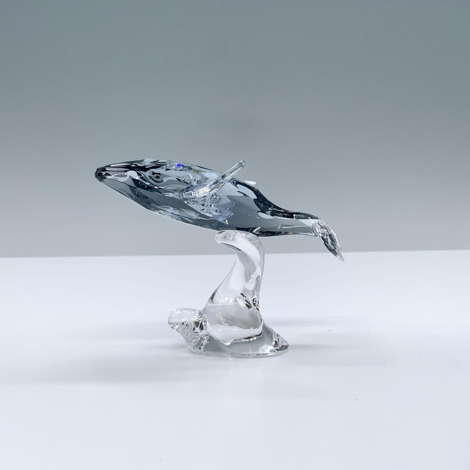 Swarovski Crystal Society Figurine, Young Humpback Whale: 2012 Annual Edition companion figurine. Figural gleams in Shadow crystal with Crystal Moonlight fins riding a clear crystal wave. Swarovski backstamp. This item has its original box. Box measures: 7"L