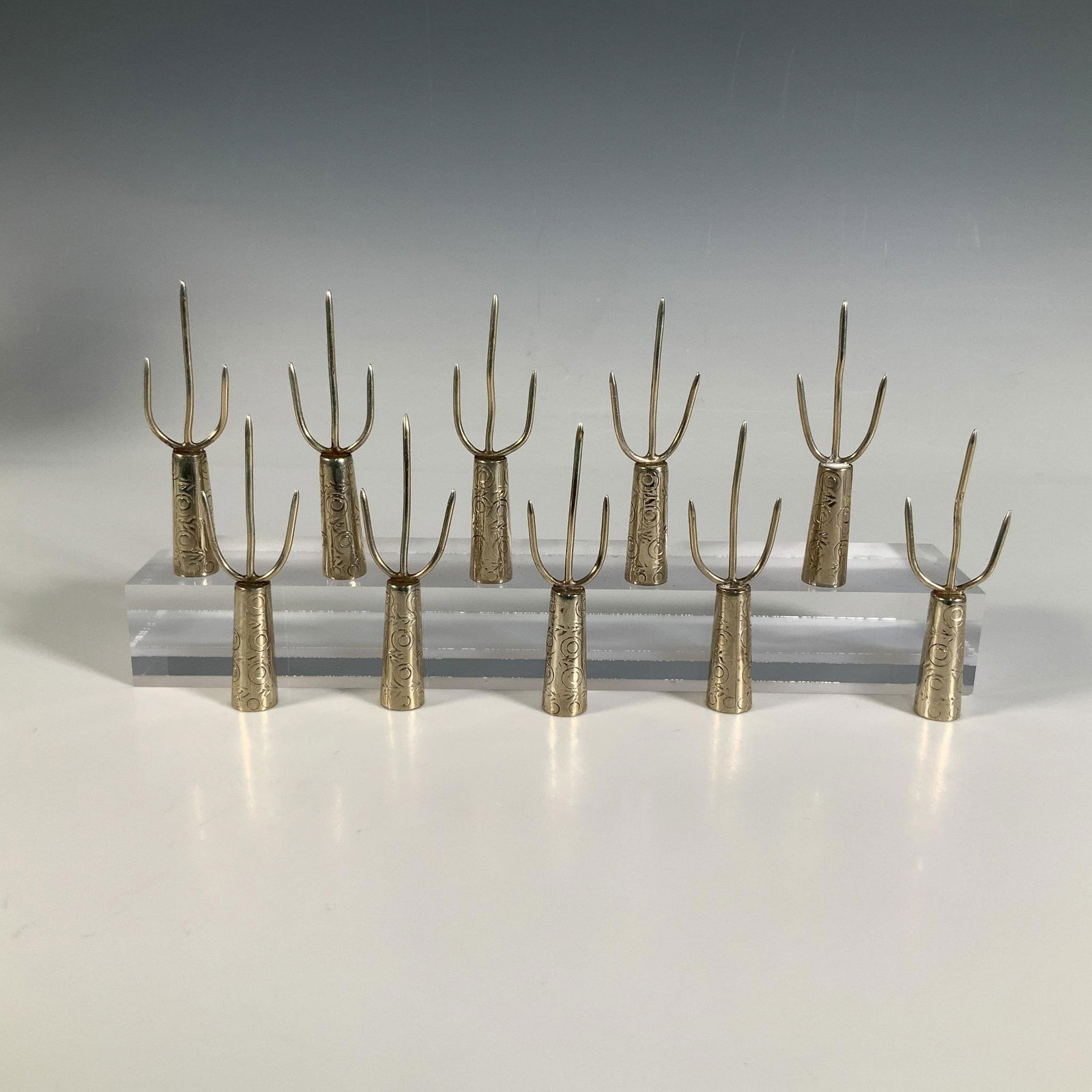 10pc Alpaca Corn Picks/Holders: This collection of ten small utensils, crafted from alpaca metal, features three prongs and is adorned with intricate circular and leaf patterns. Alpaca marking. Each pick measures: 3.5"L x 1"W x 0.5"