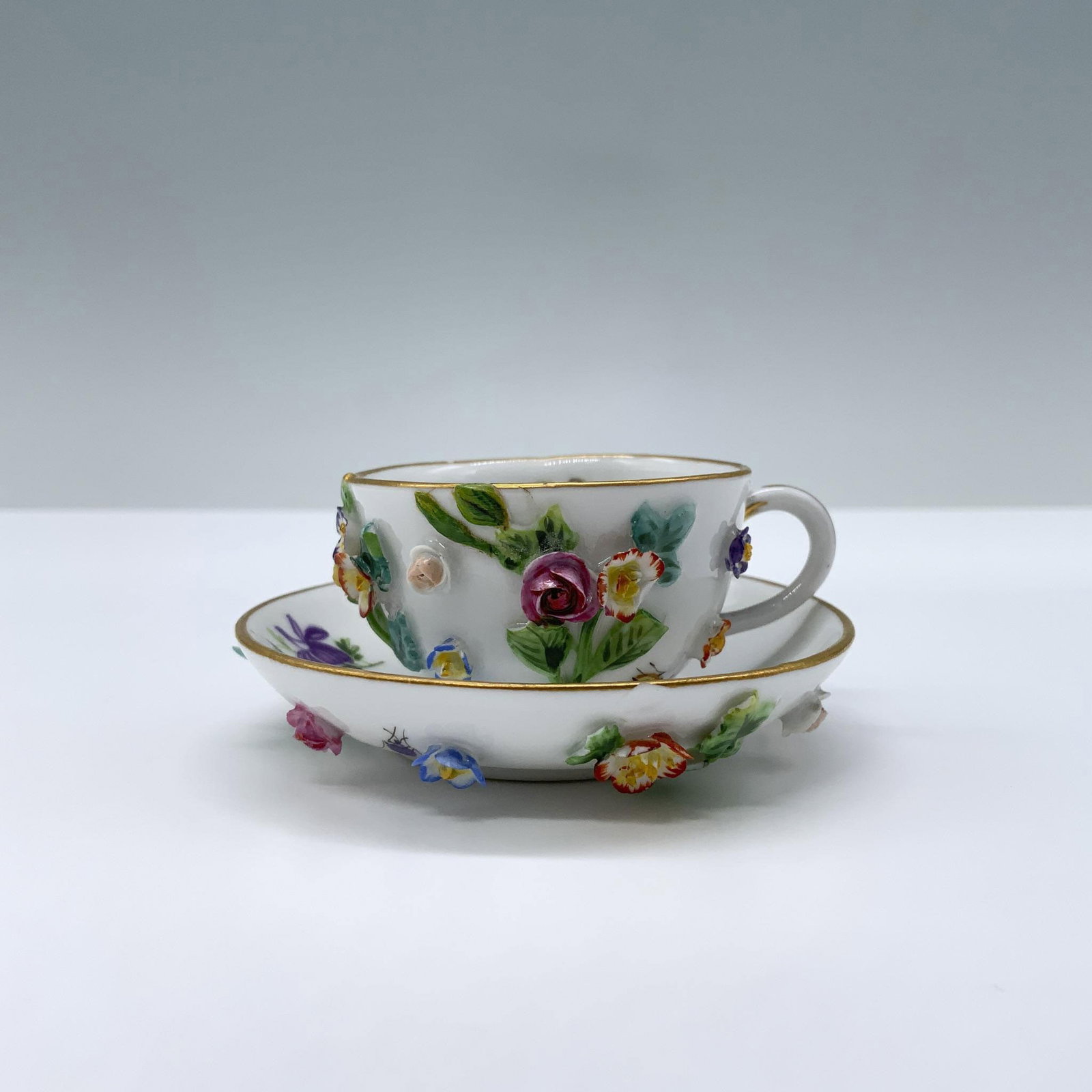 Antique Meissen Porcelain Miniature Cup & Saucer: Hand painted colorful flowers design in a mini size cup, featuring a stunning high relief flowers with gilded rim, is accompanied by a matching saucer. Meissen backstamp. Cup measures: 2"Lx 1.5"W x 0.