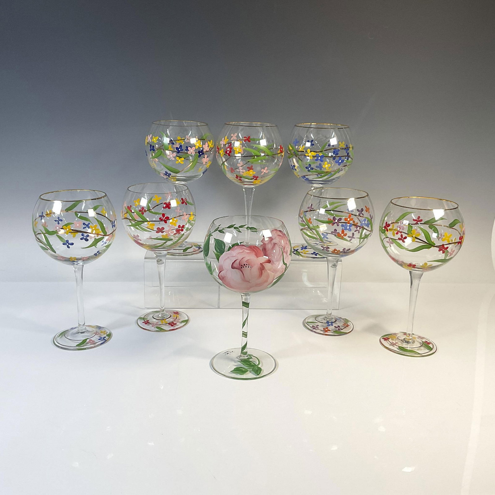 8pc Hand Painted Wine Glasses: A set of eight delightful wine glasses with a bright, floral motif. Seven of the glasses have gilding around the rims. The eighth glass is decorated with a pink peony and has the initials JG signed at