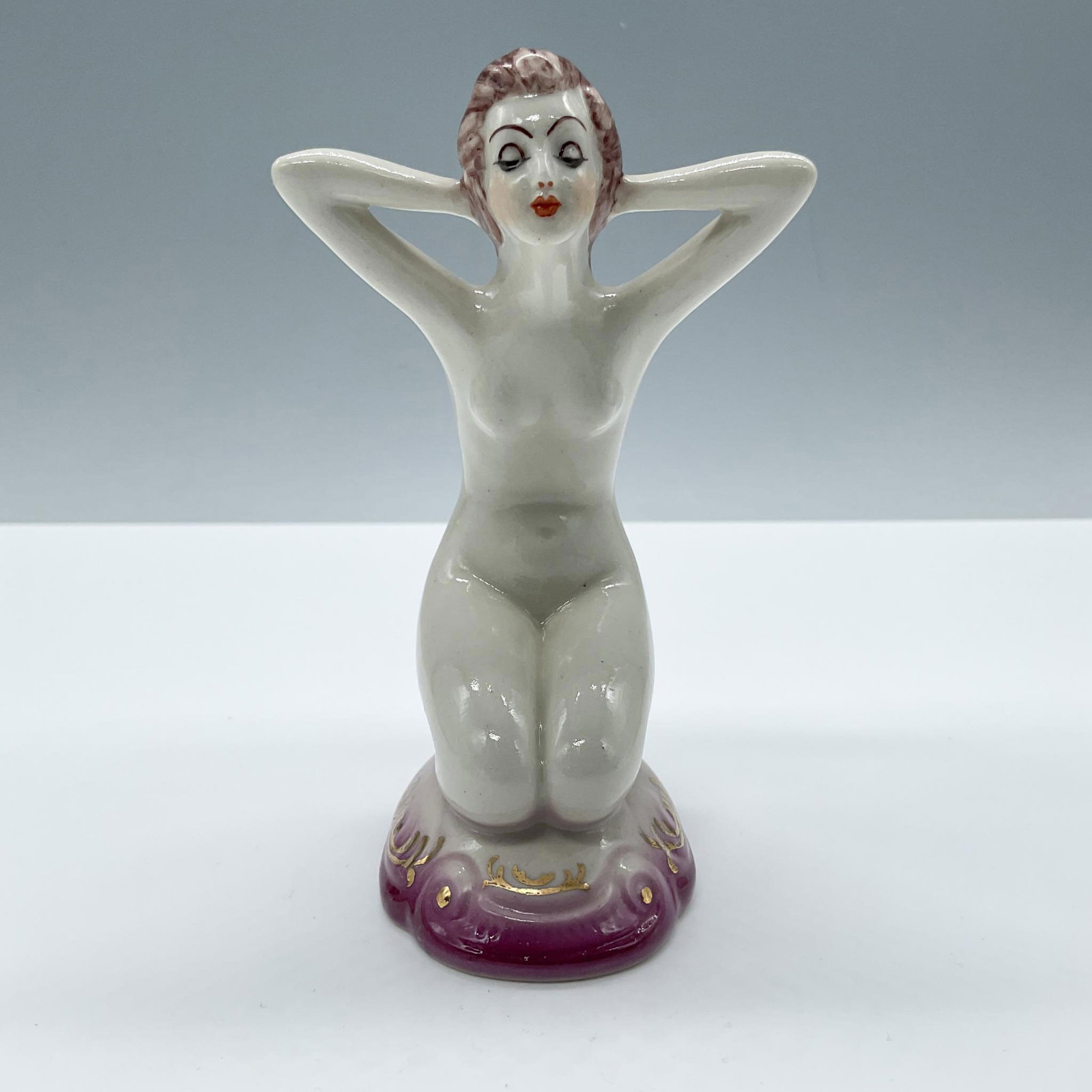 Art Deco Porcelain Nude Woman Figurine, Gilded: Beautiful hand painted figurine of a seated nude woman posing. Set on a gradient pink base, decorated with gold accents. Issued: 20th century Dimensions: 3''L x 2.75''W x 4.75''H