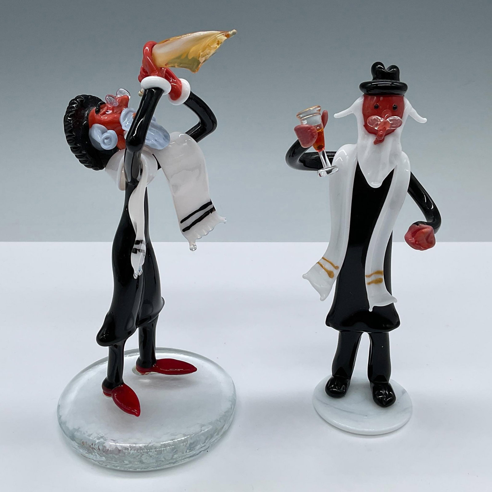 2pc Murano Glass by Moretti Raffael Rabbi Figurines: A collection of Murano Judaica art glass figures. The collection includes a Rabbi figure with a shofar, designed by Moretti Raffael (Italian, b. 1956); it figure bears Raffael MR mark. The second figu
