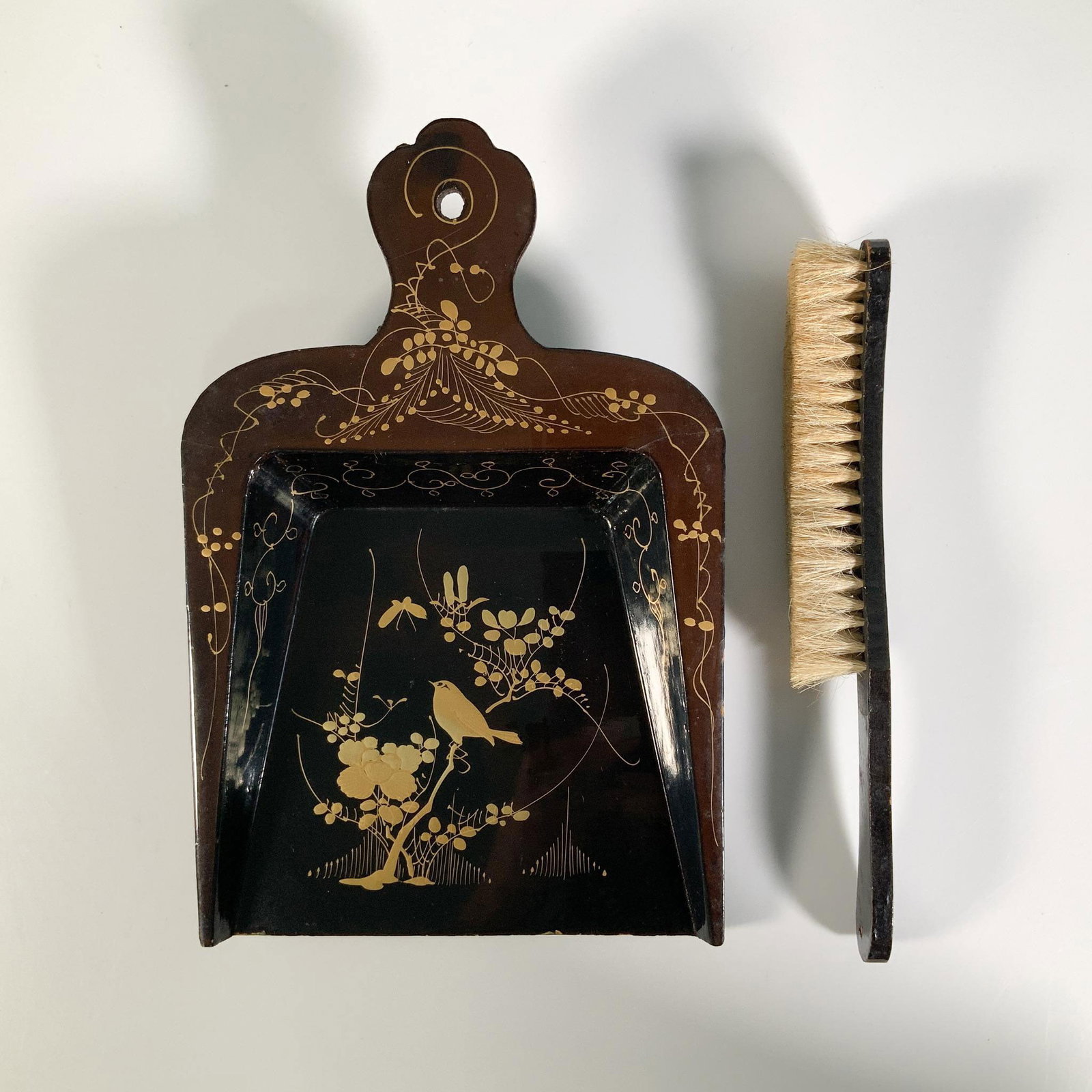 Lacquer Papier Mache Dustpan and Brush: A charming cleaning set crafted from papier mache and finished with a glossy lacquer, adorned with intricate gold-colored enamel embellishments. Largest item (dustpan): 7.5"L x 11.5"W x 2"H. Issued: 1