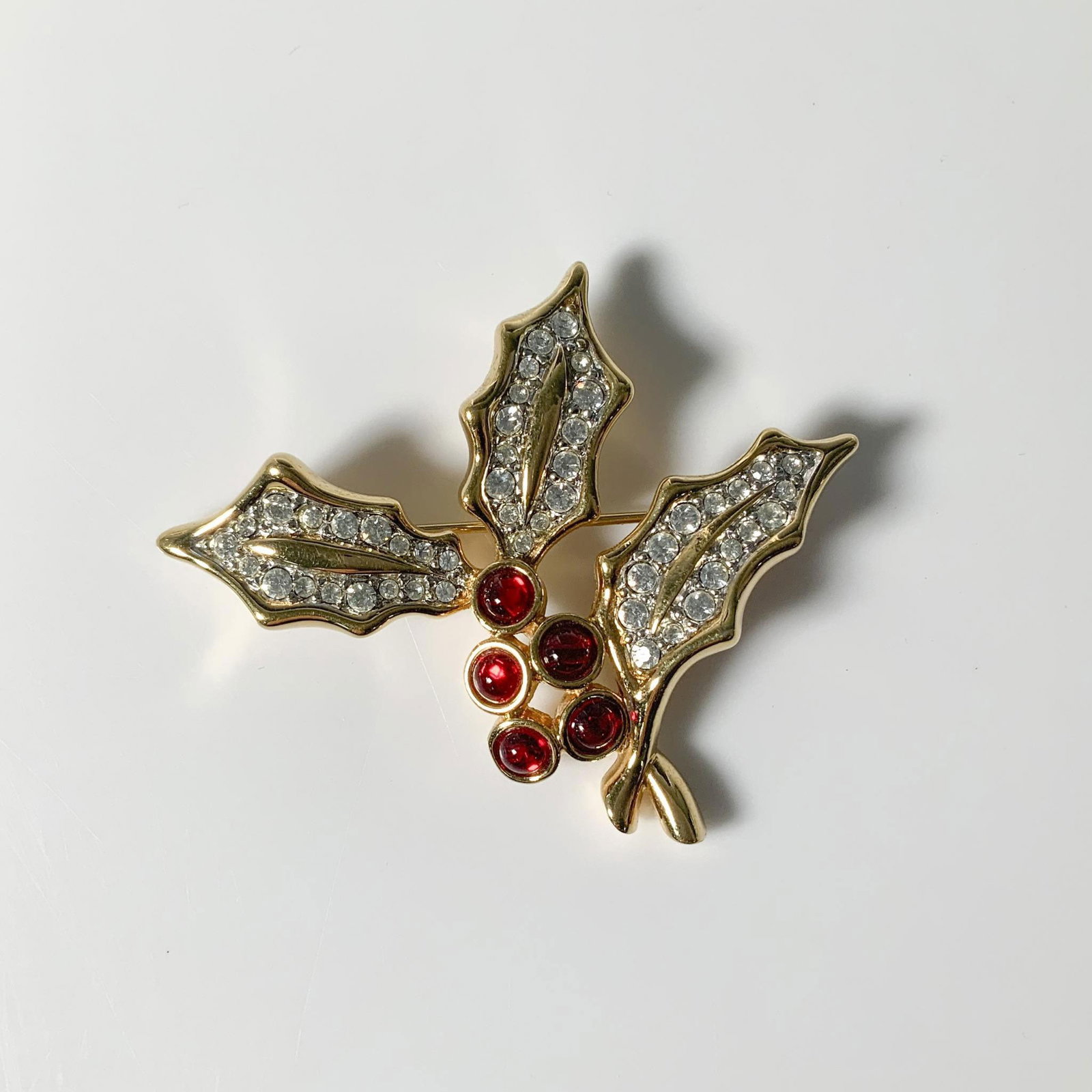 Swarovski Crystal Holly Berry Brooch Pin: A festive holly brooch pin, featuring smooth red berries and clear crystal-adorned leaves, set in a gold-tone design. Swarovski hallmark. Dimensions: 2.25"L x 2"W x 0.25"H Manufacturer: Swarovski