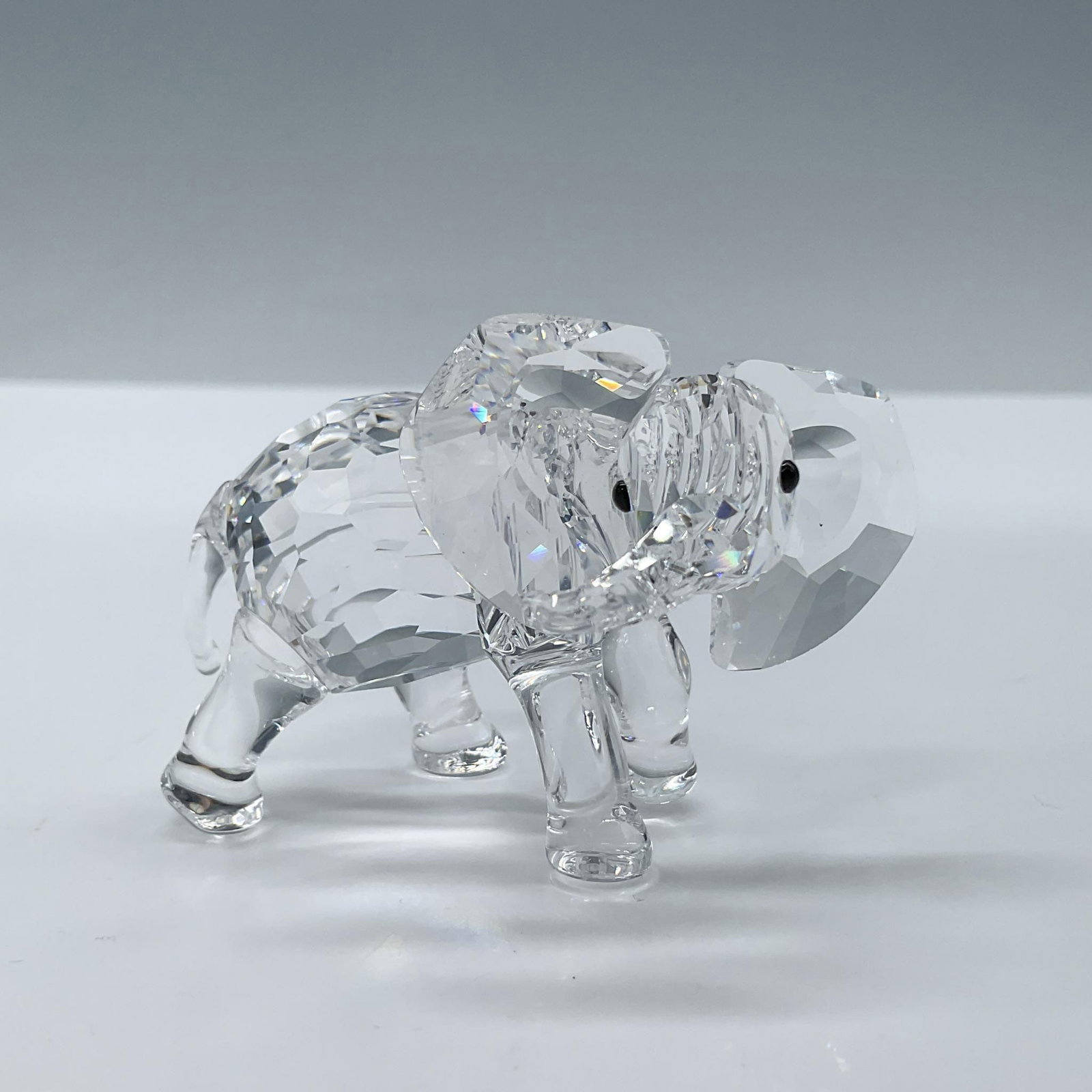 Swarovski Crystal Figurine, Little Elephant: Beautiful faceted clear crystal baby elephant figure with jet black eyes. Swarovski acid backstamp. This item has its original box, dimensions: 4.5''H x 3.5''dia. Artist: Heinz Taberstshofer Issued: 2