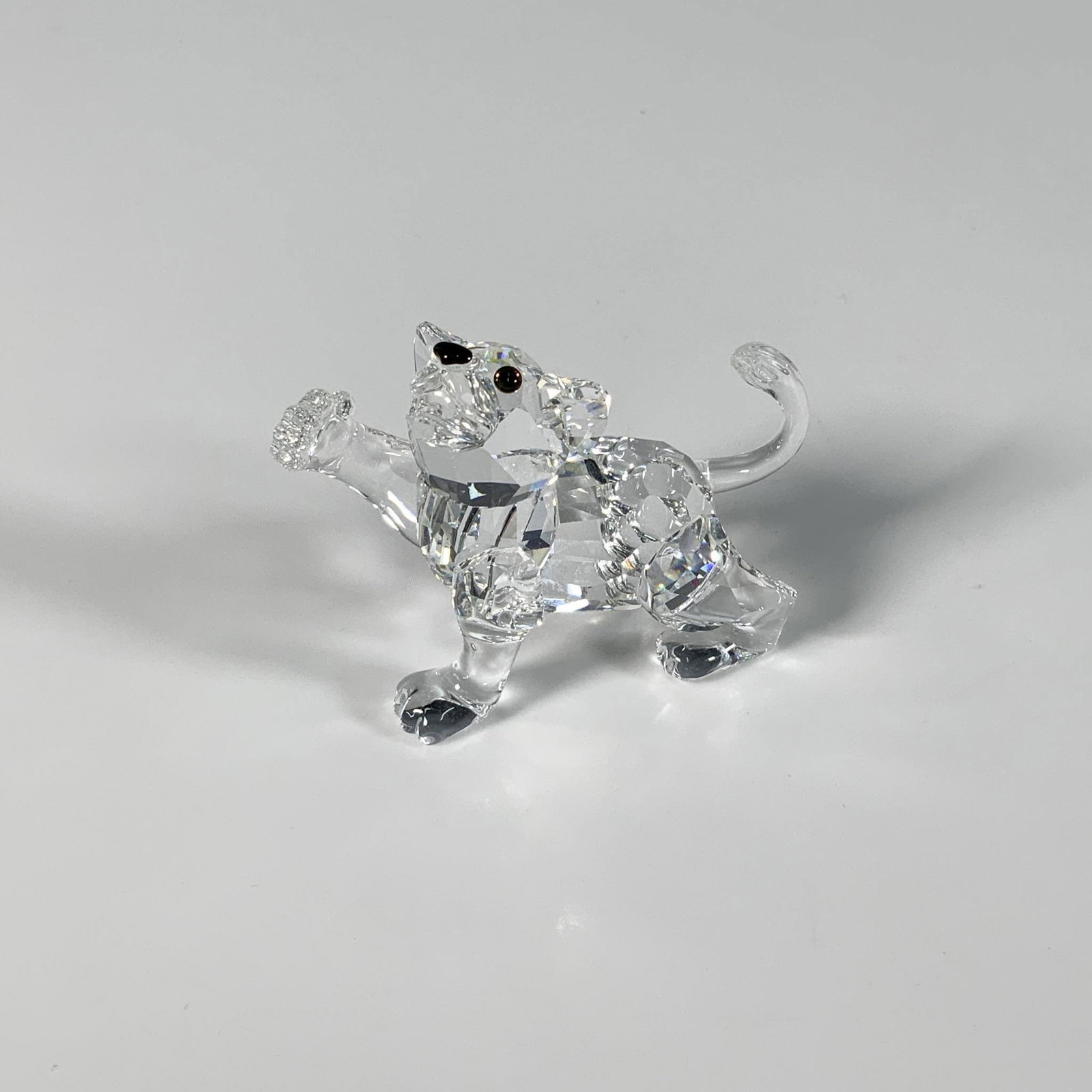Swarovski Silver Crystal Figurine, Lion Cub: A dazzling precision-cut figure of a baby lion with its arm stretched out, adorned with a black nose and iridescent eyes. Part of the African Wildlife group. Swarovski mark. This item has its original