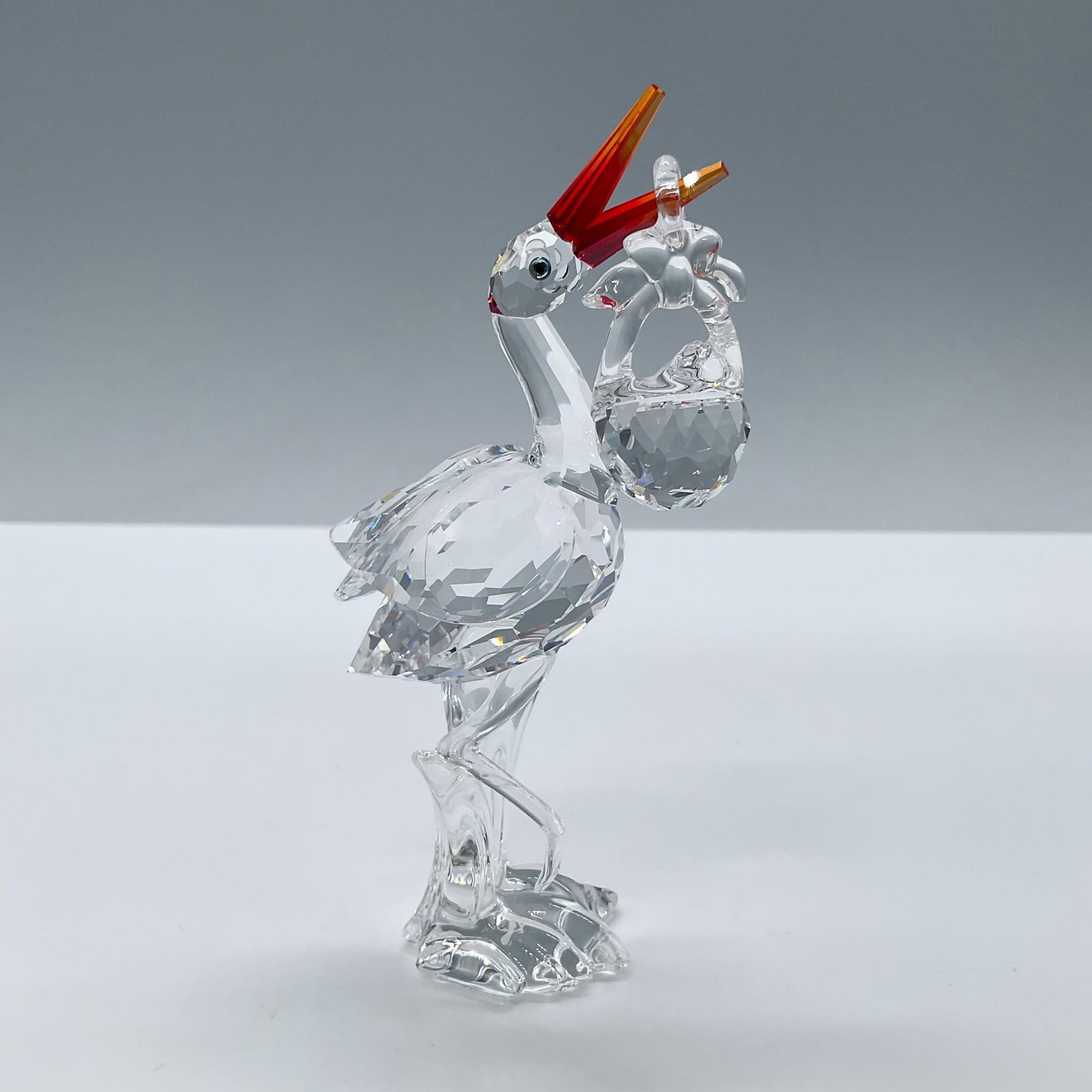 Swarovski Crystal Figurine, Stork with Baby: Beautiful clear crystal stork with a dark red beak, accompanied by a clear crystal baby basket. Swarovski acid backstamp. Includes the original box, dimensions: 6''L x 6''W x 3.75''H. Artist: Gabriele