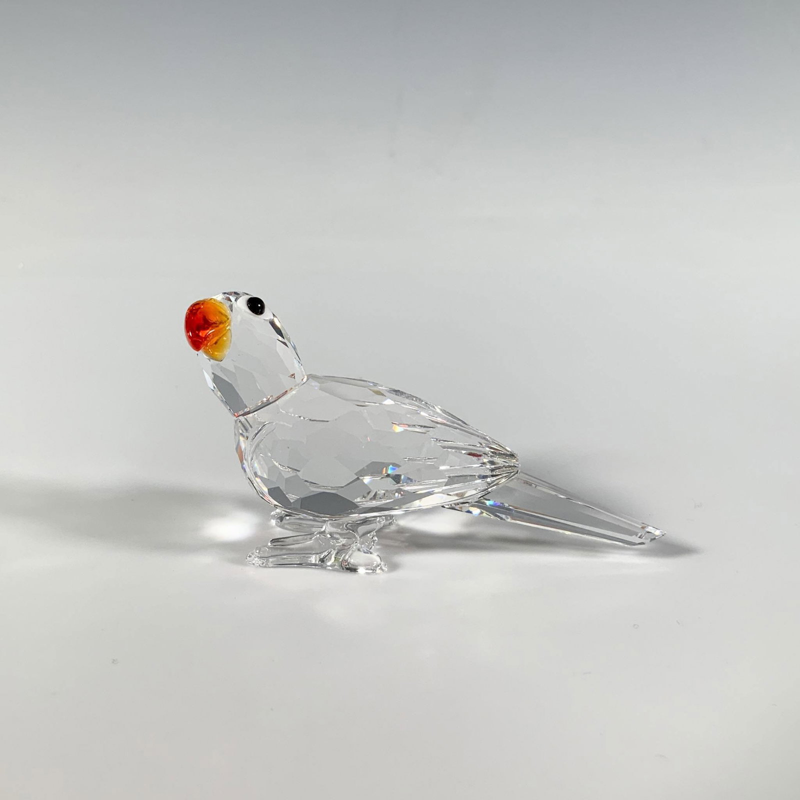Swarovski Crystal Figurine, Parrot: A small faceted figure of an adorable parrot with a vibrant orange beak and black eyes. Part of the Feathered Beauties collection. Swarovski marking. This item has its original box: 3.25"W x 4.75"H. A
