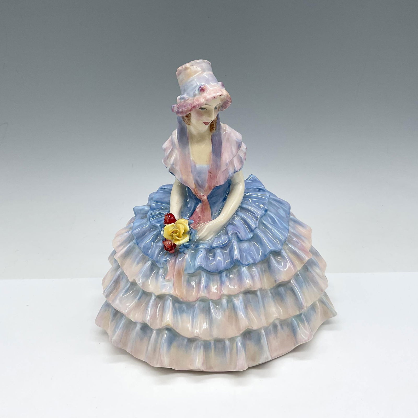 Chloe - HN1479 - Royal Doulton Figurine: Young figure in ruffled, tiered dress colored in pink and blue with matching bonnet. Royal Doulton backstamp. Artist: Leslie Harradine Issued: 1931 - 1949 Dimensions: 5.5"L x 4.5"W x 5.5"H Manufacture