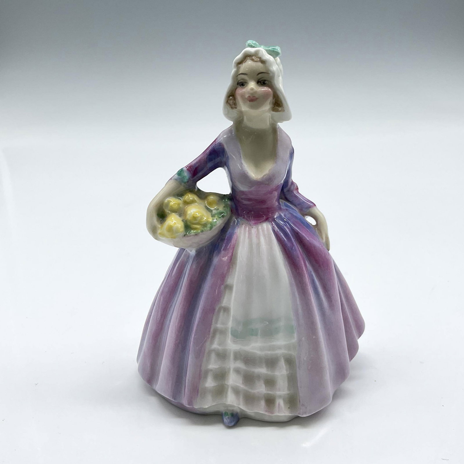Janet - M75 - Royal Doulton Figurine: Part of the M series for Pretty Ladies, colored in purple carrying basket of flowers. Royal Doulton backstamp. Artist: Leslie Harradine Issued: 1936 - 1949 Dimensions: 4"H Manufacturer: Royal Doulton 