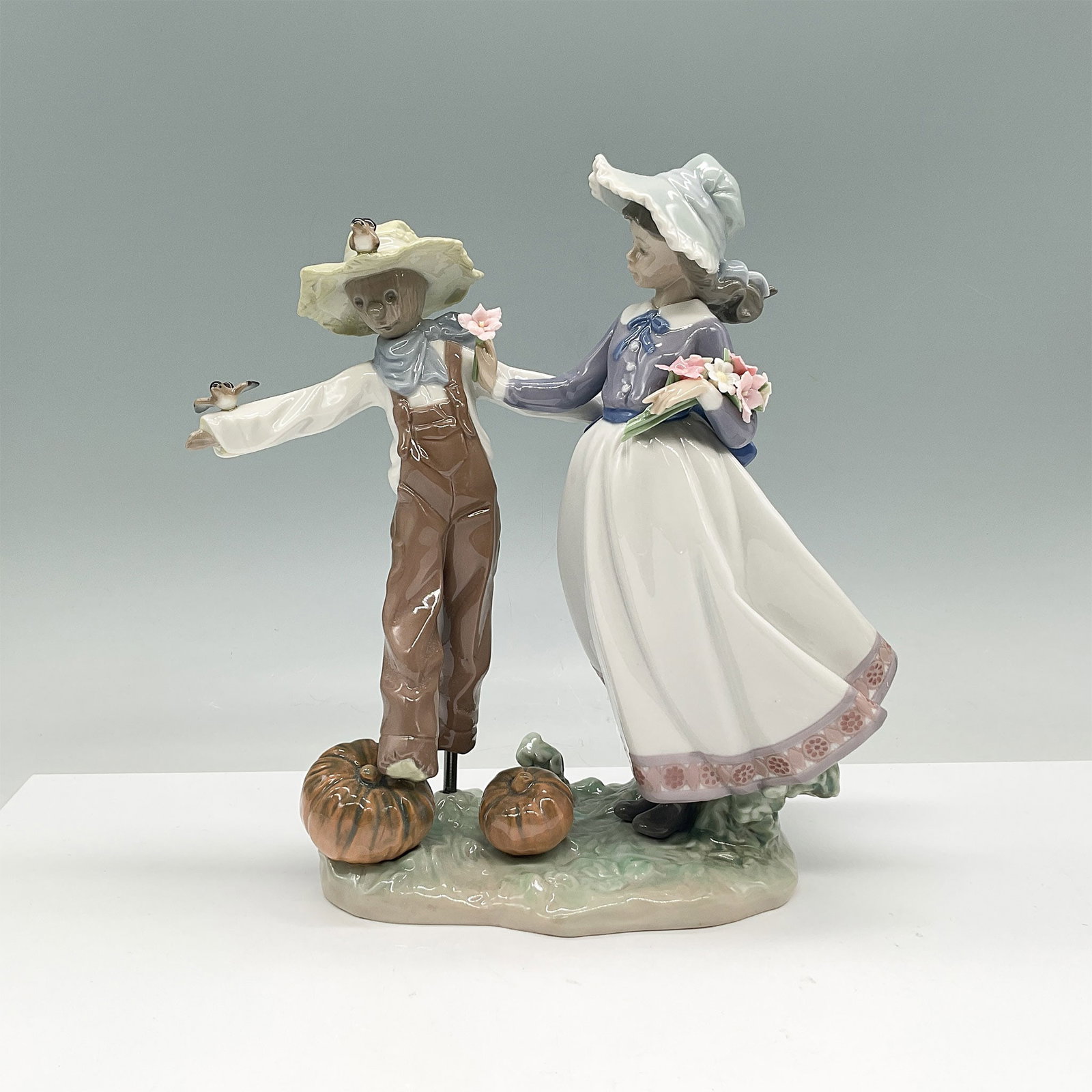 Lladro Porcelain Figurine, Scarecrow and the Lady 01005385: Presenting the Lladro Scarecrow and the Lady figurine, model 01005385. Sculpted by Regino Torrijos, this charming piece was introduced in 1986 and retired in 1996. The figurine features a young woman 