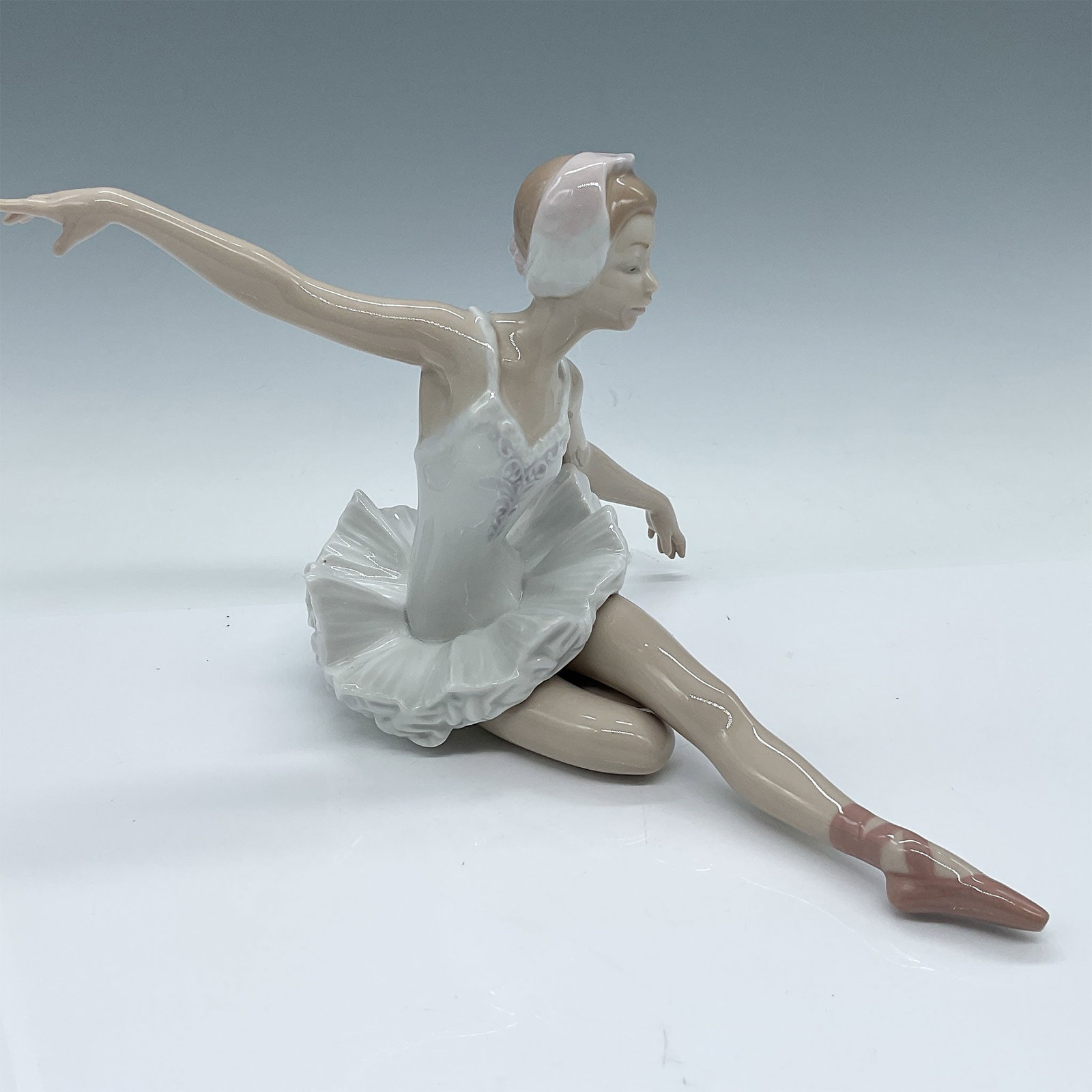 Lladro Porcelain Figurine, Swan Ballet 01005920: Lladro porcelain figurine titled "Swan Ballet". This stunning piece depicts a graceful ballerina in a stretching pose, meticulously crafted with fine details in her flowing tutu and delicate form. Mea