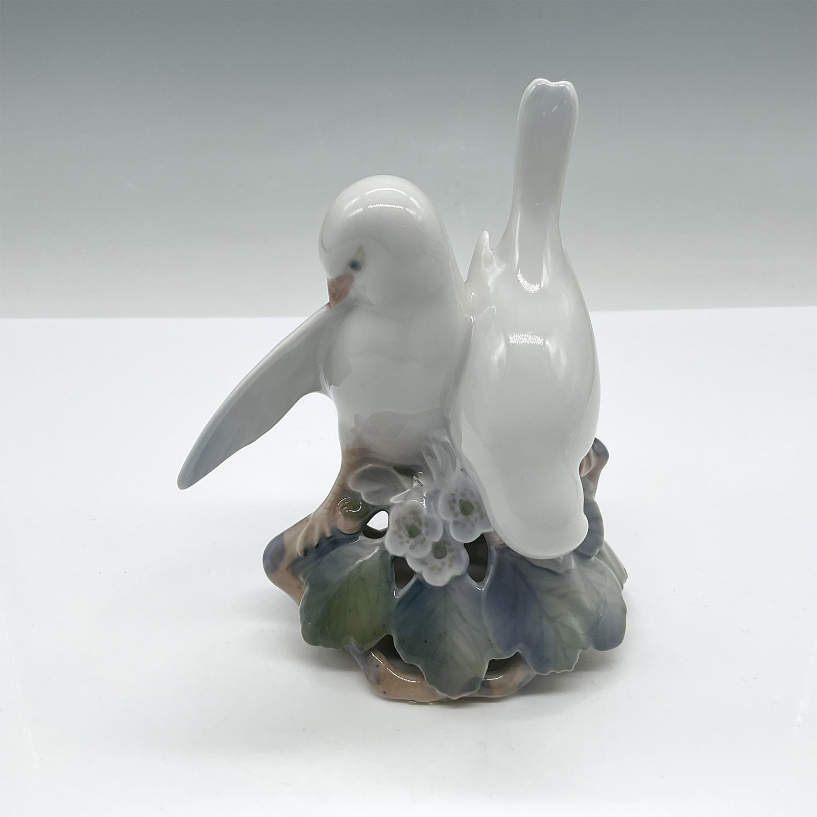 Royal Copenhagen Figurine, Lovebirds: A Royal Copenhagen porcelain figurines perched among floral details, showcasing the brand's signature delicate craftsmanship and hand-painted accents. Designed in subtle pastel tones, this piece exemp