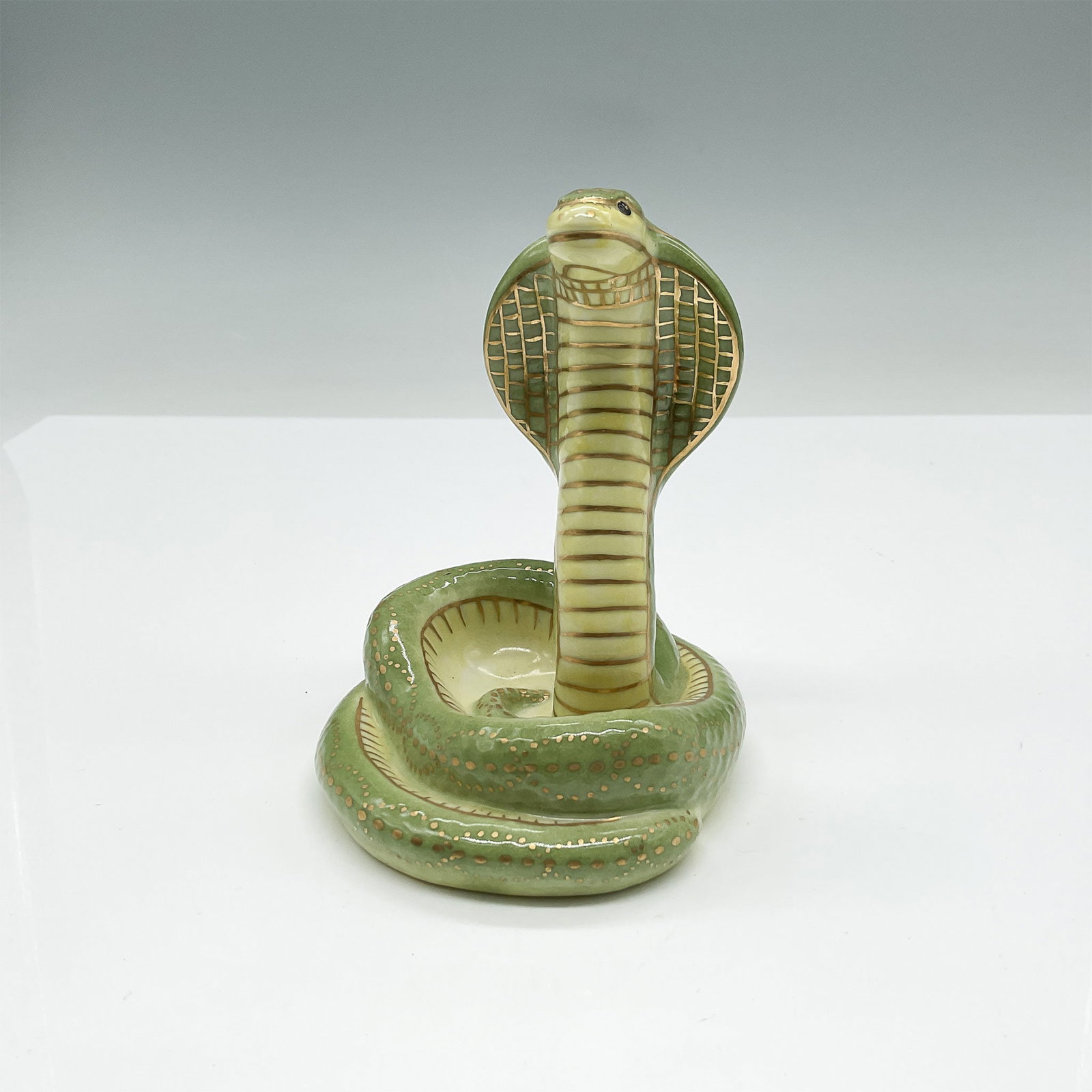 Herend Porcelain Cobra Figurine: A striking Herend Hungary handpainted cobra figurine crafted from porcelain and adorned with exquisite green and gold accents. The detailed craftsmanship showcases the cobra's coiled body, raised hood