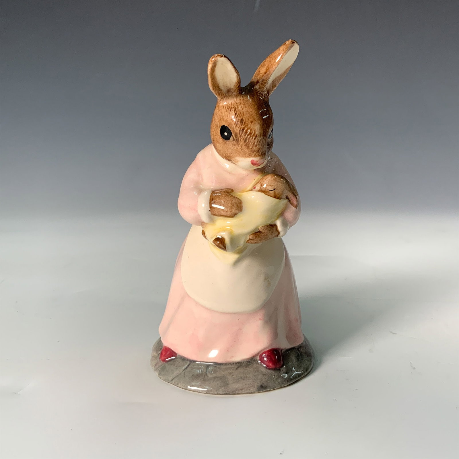 Royal Doulton Bunnykins Figurine, Mother and Baby DB167: This delightful Royal Doulton Bunnykins figurine, titled Mother and Baby, depicts a charming scene of a mother rabbit tenderly holding her baby. Crafted in fine bone China, it features hand-painted de