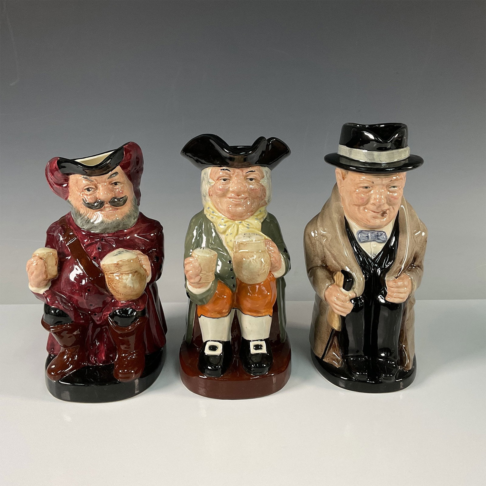 3pc Royal Doulton Large Toby Jugs Designed by Harry Fenton: A delightful collection of three Royal Doulton Toby Jugs, each meticulously designed by the renowned artist Harry Fenton. This set includes: 'Falstaff', depicting the merry knight from Shakespeare's p