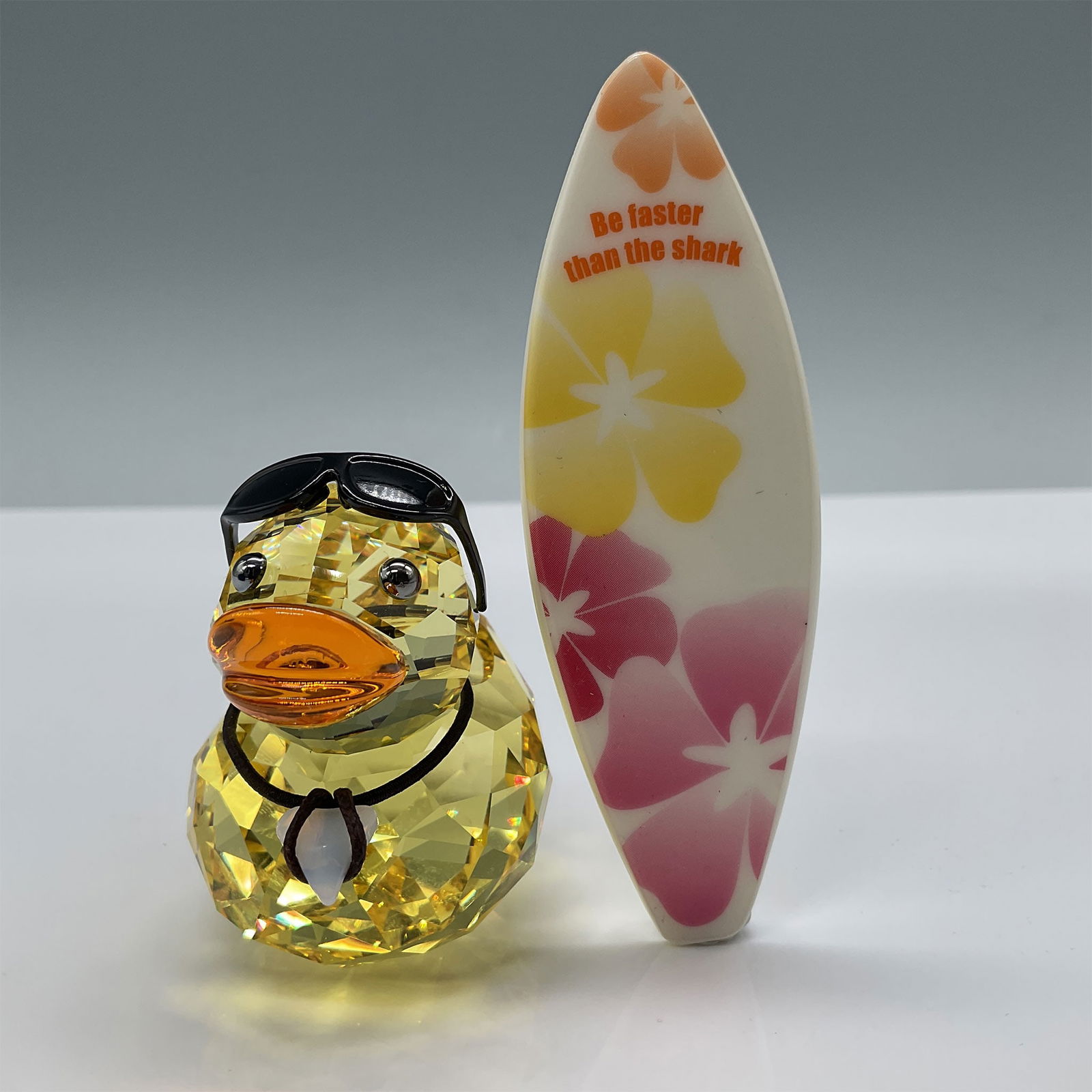 Swarovski Crystal Figurine, Sunny Steve with Box: Swarovski crystal figurine titled "Sunny Steve," a cheerful yellow duck accessorized with a shark tooth necklace, sunglasses, and a surfboard. Measures approximately 2"H and is accompanied by its orig