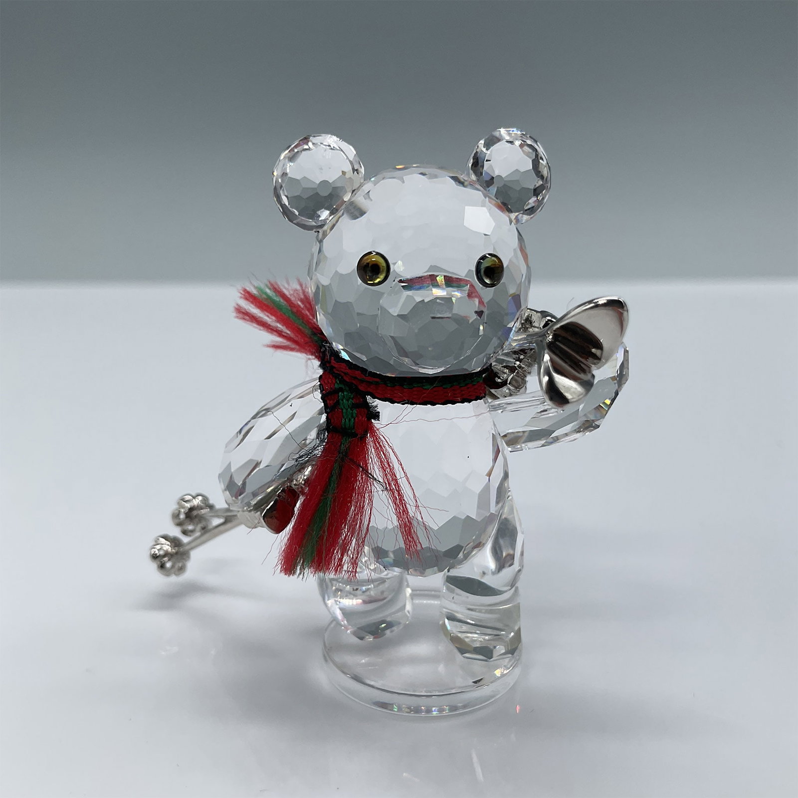 Swarovski Crystal Figurine, Kris Bear with Skis: Swarovski crystal figurine titled "Kris Bear with Skis," featuring a charming bear holding skis and ski poles, accented with a red and green scarf. The figurine stands approximately 2"H and includes t