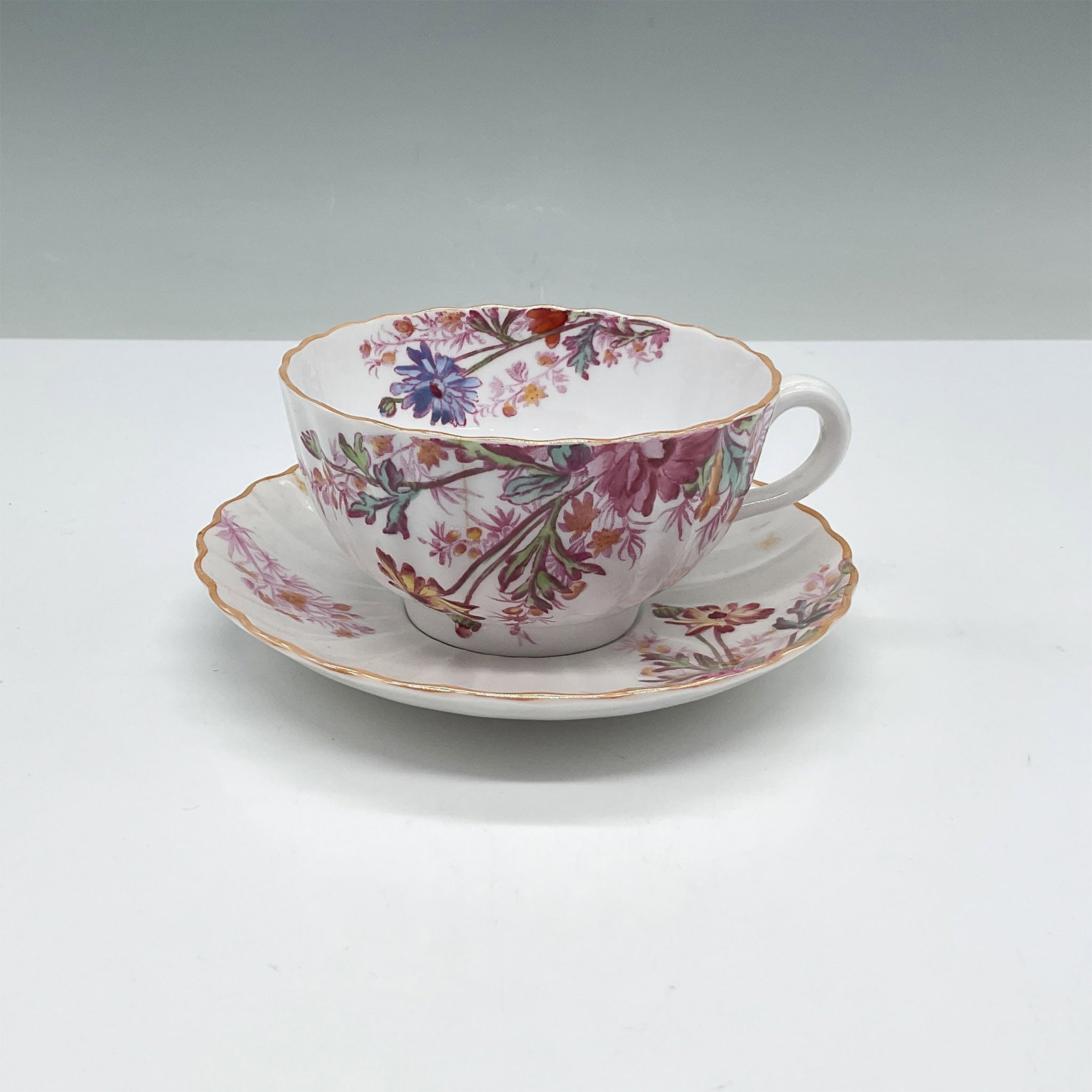 2pc Spode Chelsea Garden Bone China Teacup and Saucer Set: A beautiful Spode Chelsea Garden teacup and saucer set crafted from fine bone china in England. Featuring a scalloped rim and a vibrant floral pattern with accents of pink, blue, and green, this set e