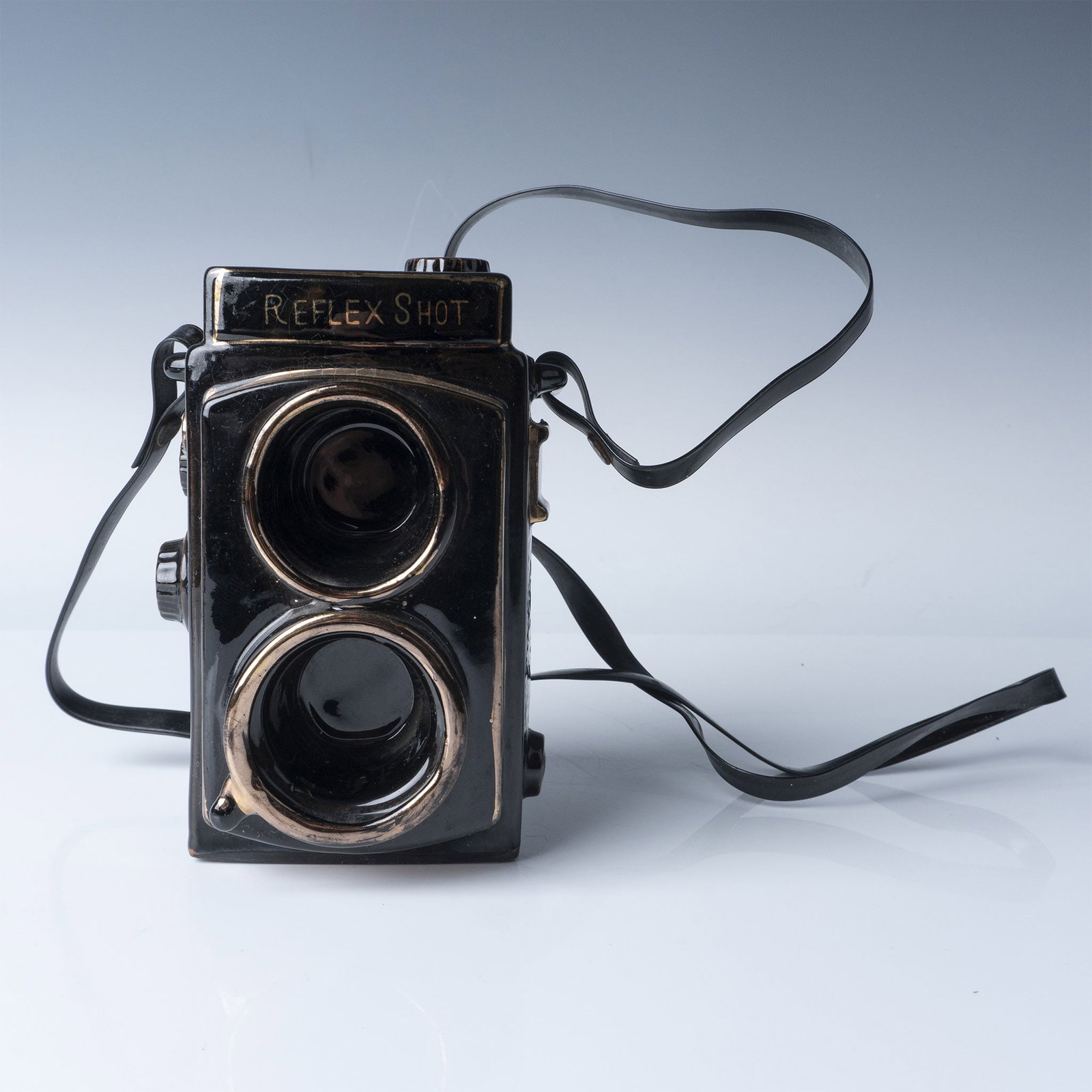 Ceramic Reflex Camera Figurine, Black and Copper Tone: Charming ceramic figurine designed to resemble a vintage twin-lens reflex camera. Features a glossy black glaze with copper-tone highlights, including intricate detailing and a sculpted strap. Stamped