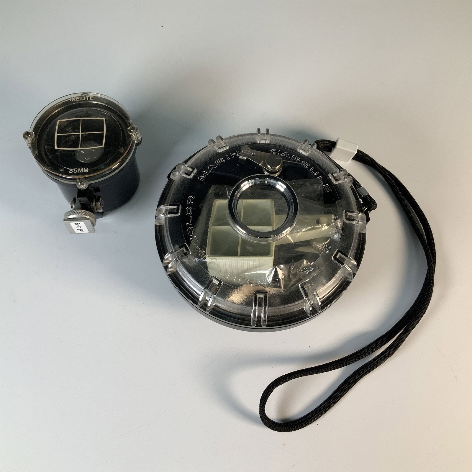 2pc Ikelite Underwater Camera Housing & Hi-Color Capsule: A pair of vintage underwater photography accessories including an Ikelite 35mm underwater camera housing and a Hi-Color Marine Capsule. The Ikelite housing features a robust clear acrylic design for u