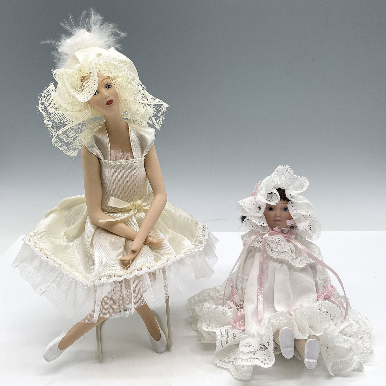 2pc Vintage 1950s Porcelain Display Dolls: Dressed in period clothing, an elegant woman is seated dressed in wide brim hat in short, ruffled skirt dress 4"L x 2"W x 9"H and young girl all in white 4"L x 3"W x 4.5"H. Issued: 20th century Dimens