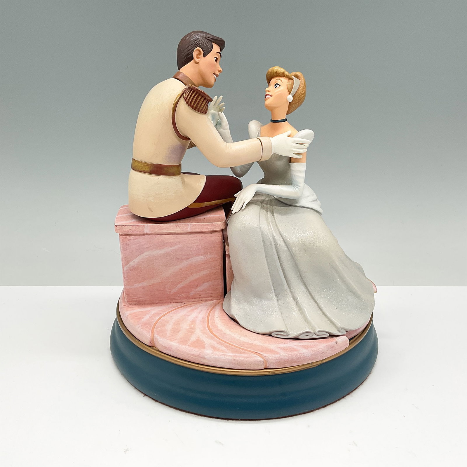 Disney Cinderella and Prince Charming Keepsake Box Figurine: A delightful Disney figurine depicting Cinderella and Prince Charming in an intimate moment, seated on a decorative pink and teal base, which doubles as a hidden keepsake box. The sculpture features i