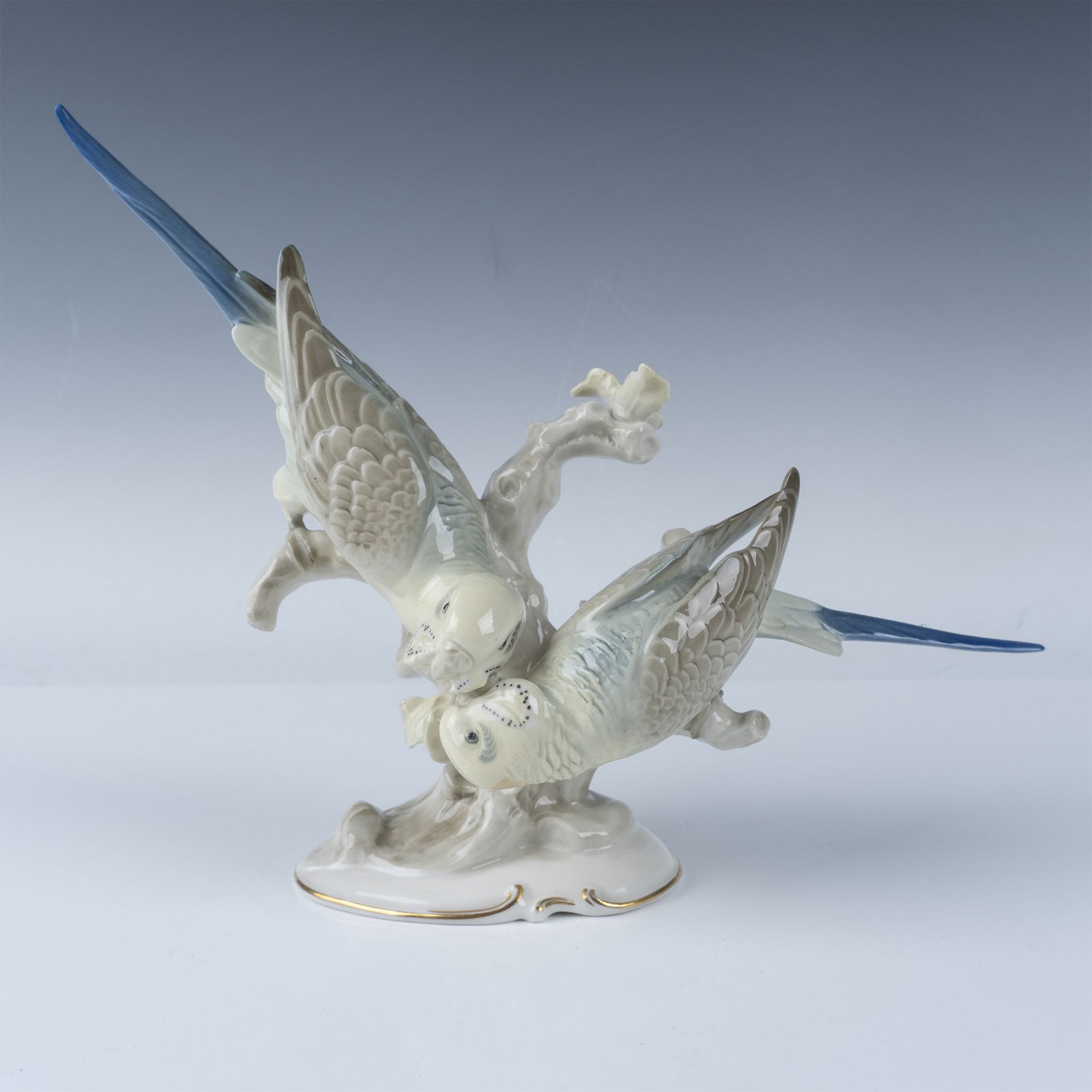 Hutschenreuther Porcelain Parakeet Figurine: Glossy porcelain figurine depicting two parakeets perched on a delicately sculpted branch. Hutschenreuther backstamp and artist marking on base. Artist: K. Tutter Issued: 20th century Dimensions: 4.5"