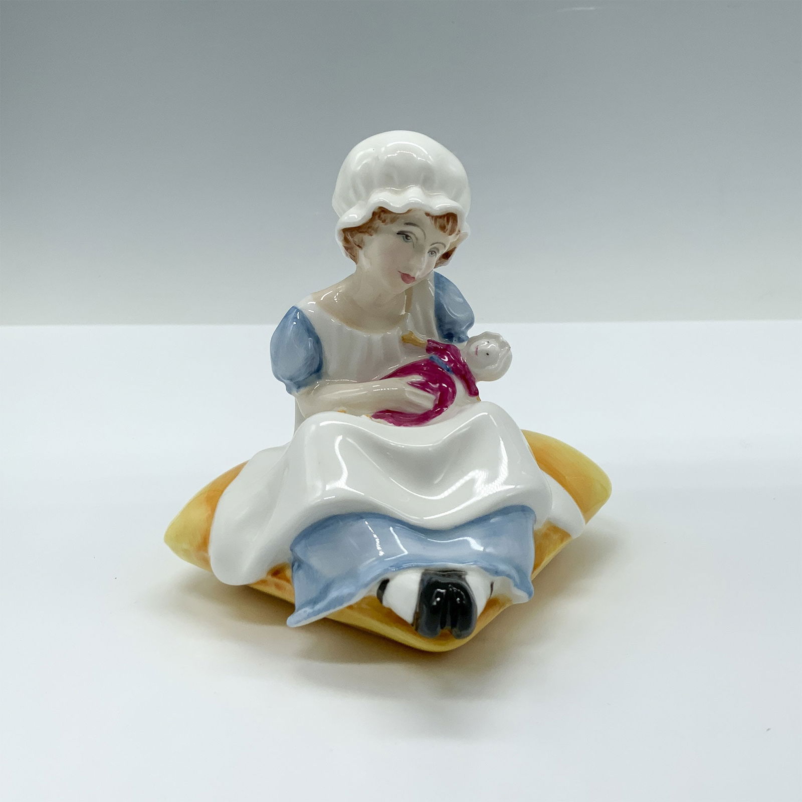 Royal Doulton Bone China Figurine, Ellen HN3020: This figure of a girl in an apron and bonnet holding her doll from the Kate Greenaway Collection is based of one of Kate's books named Under The Window which contains idyllic verses concerning childre