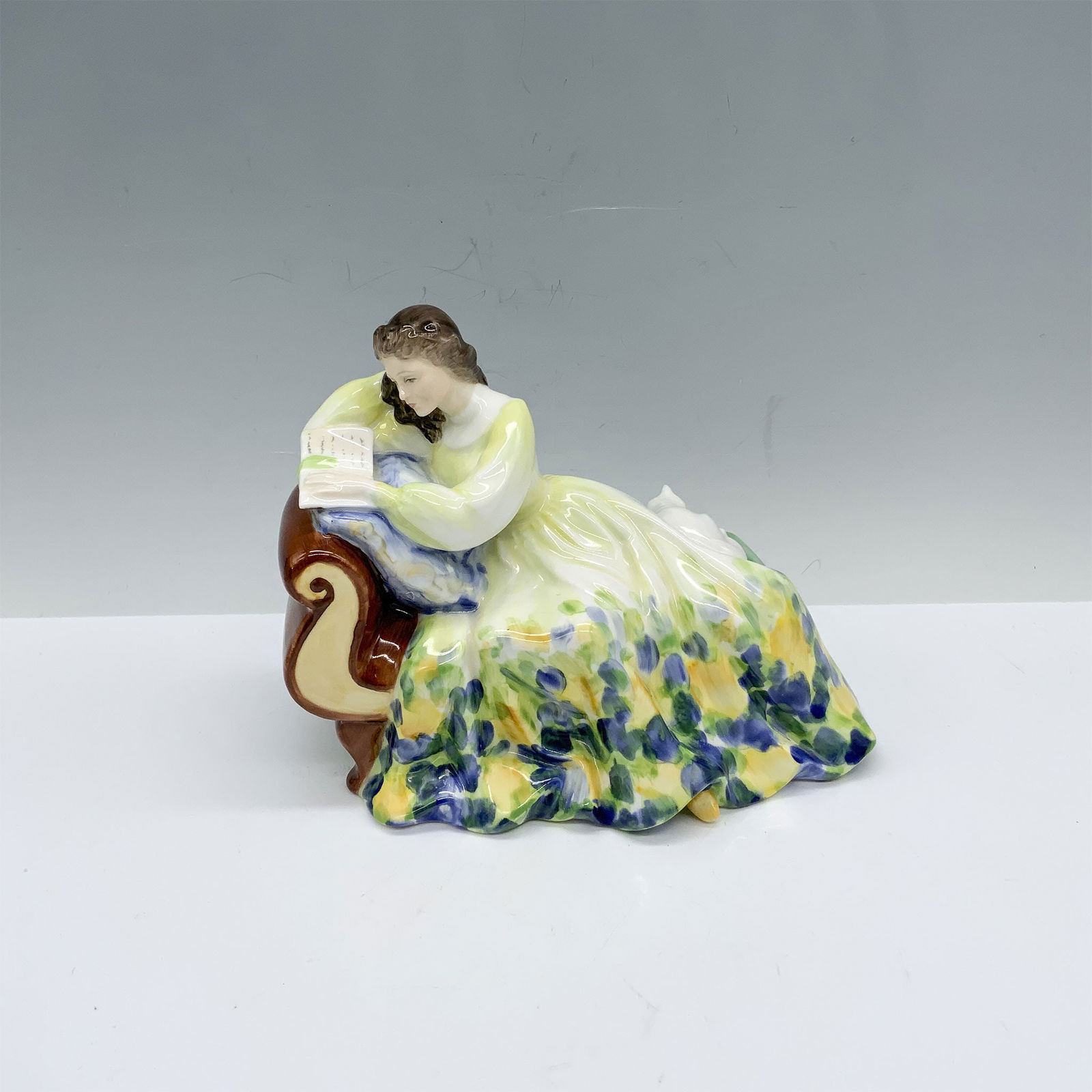 Royal Doulton Bone China Figurine, Solitude HN2810: Handmade and hand decorated glossy figure featuring a woman enjoying her time alone as she rests with her cat, enjoying a good book. Royal Doulton backstamp. Artist: Peggy Davies Issued: 1977-1983 Dim