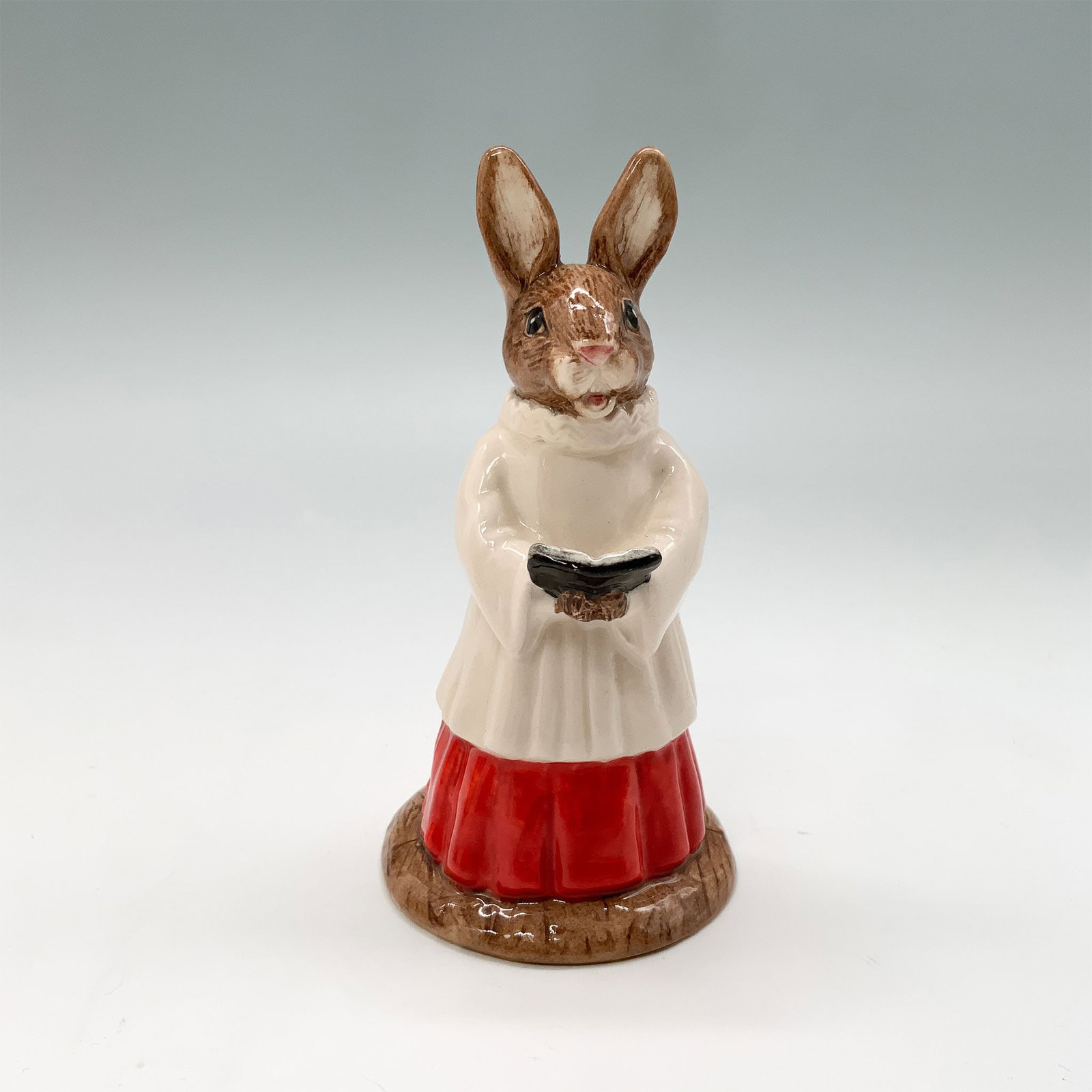 Royal Doulton Bunnykins Figurine, Choir Singer DB223: A charming Royal Doulton Bunnykins figurine titled Choir Singer, model number DB223. This hand-decorated porcelain figurine features a bunny dressed in a choir robe holding a hymn book. Includes the o