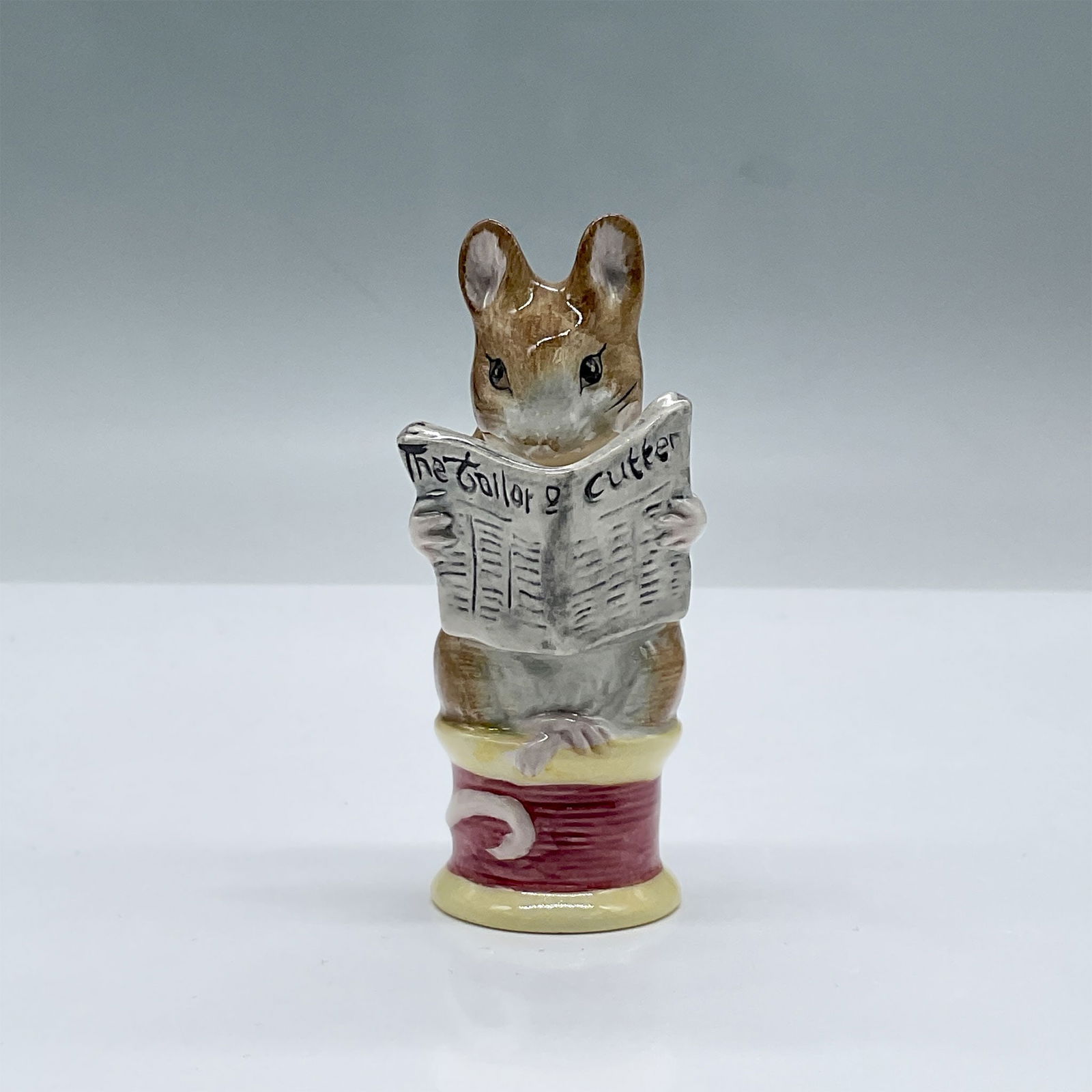 Royal Albert Beatrix Potter Figurine, Tailor of Gloucester: Glossy porcelain. Features a mouse sitting on a spool of threat reading a newspaper. Royal Albert Beatrix Potter backstamp. This item has its original box, dimensions: 2.5"L x 2"W x 5"H. Issued: 1989