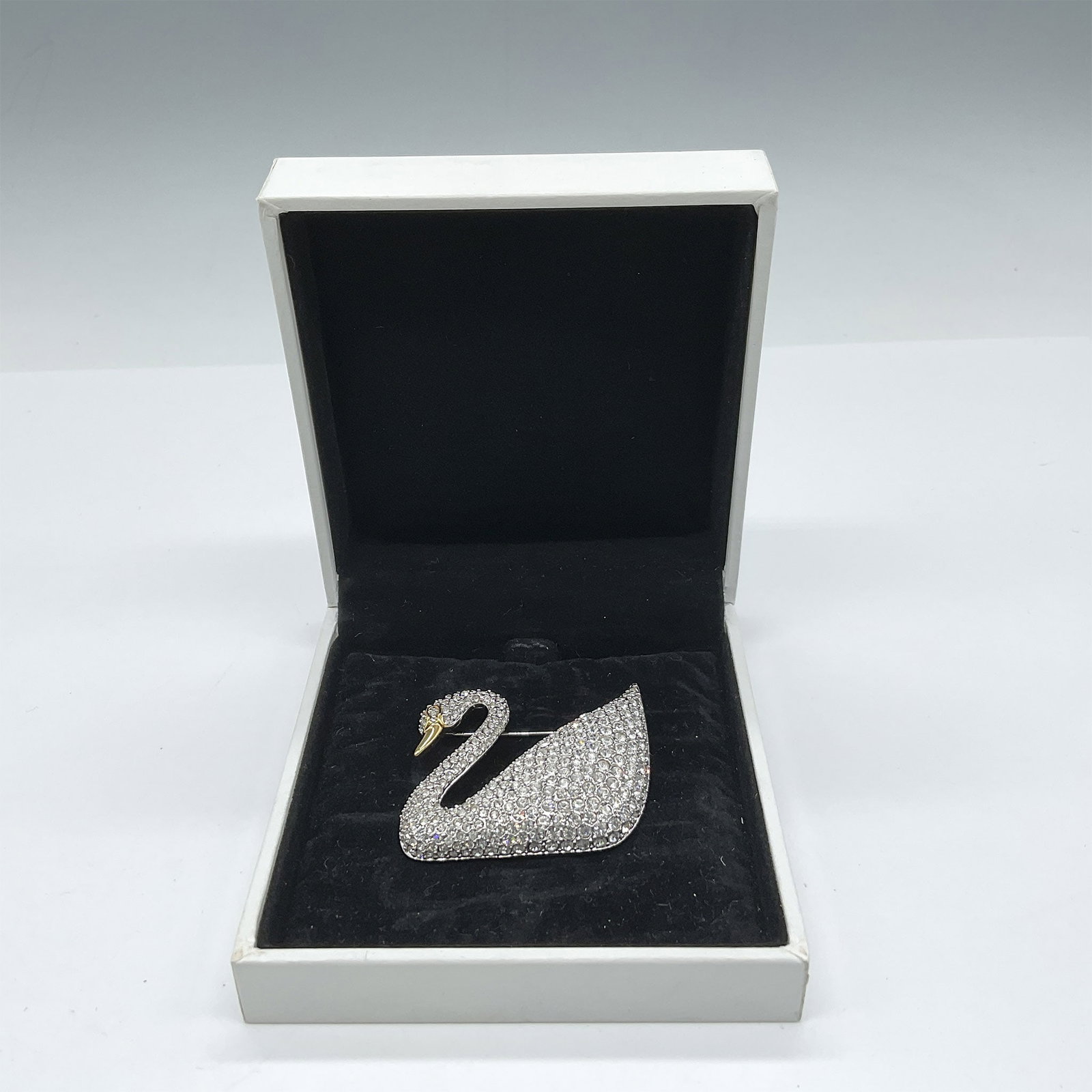 Swarovski Signature Jewelry, Swan Brooch: Swan hallmark pin created with rhinestone encrusted crystals throughout design accenting gold-toned beak and eye. Swarovski impressed mark. This item has its original box: 3.5"L x 4"W x 1.5"H. Issued: