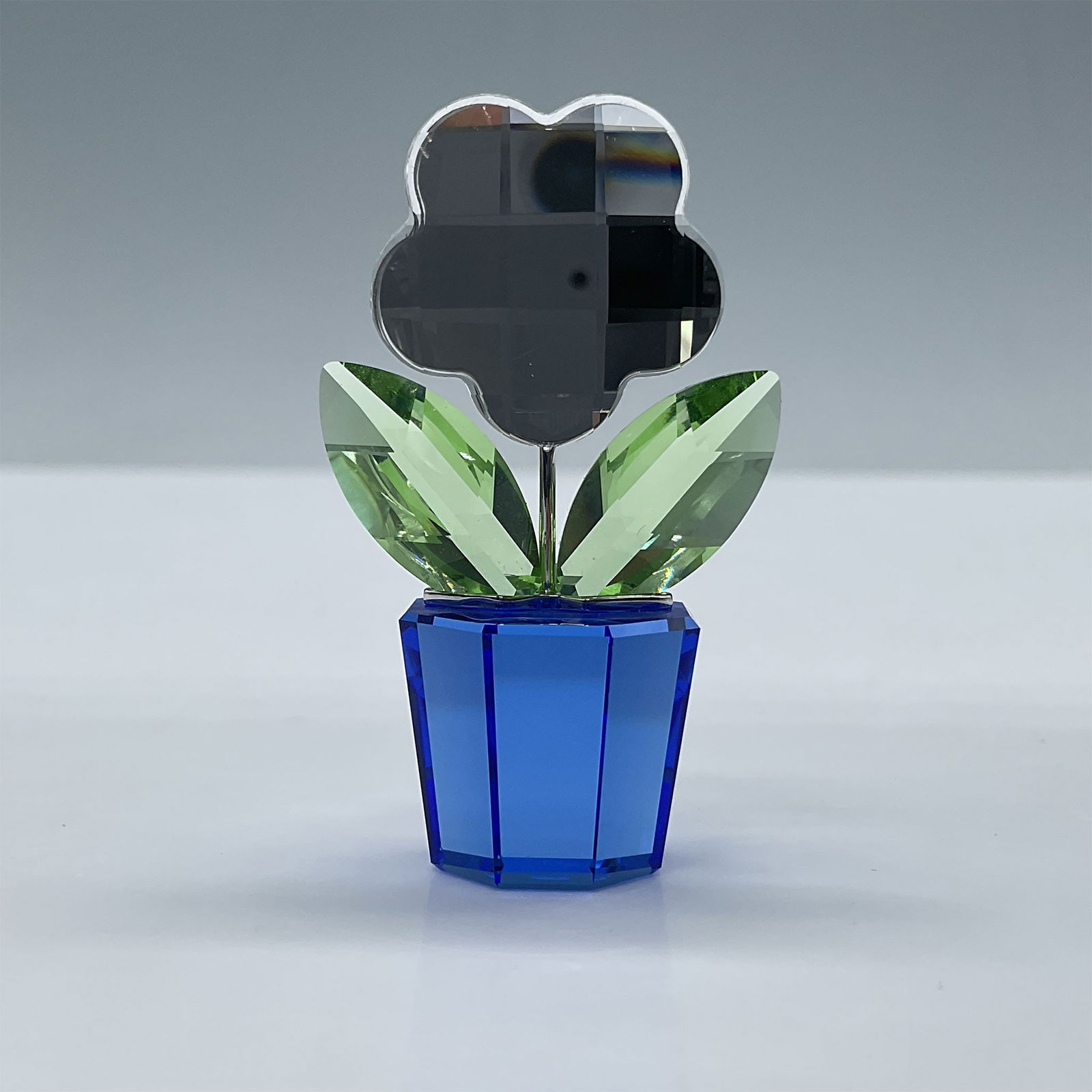 Swarovski Crystal Figurine, Flower Clear: Beautiful facetted clear flower on a sapphire blue pot with peridot green leaves. Swarovski etched backstamp. This item has its original box. Dimensions of the box: 3''L x 3''W x 1.5''H. Issued: 2006