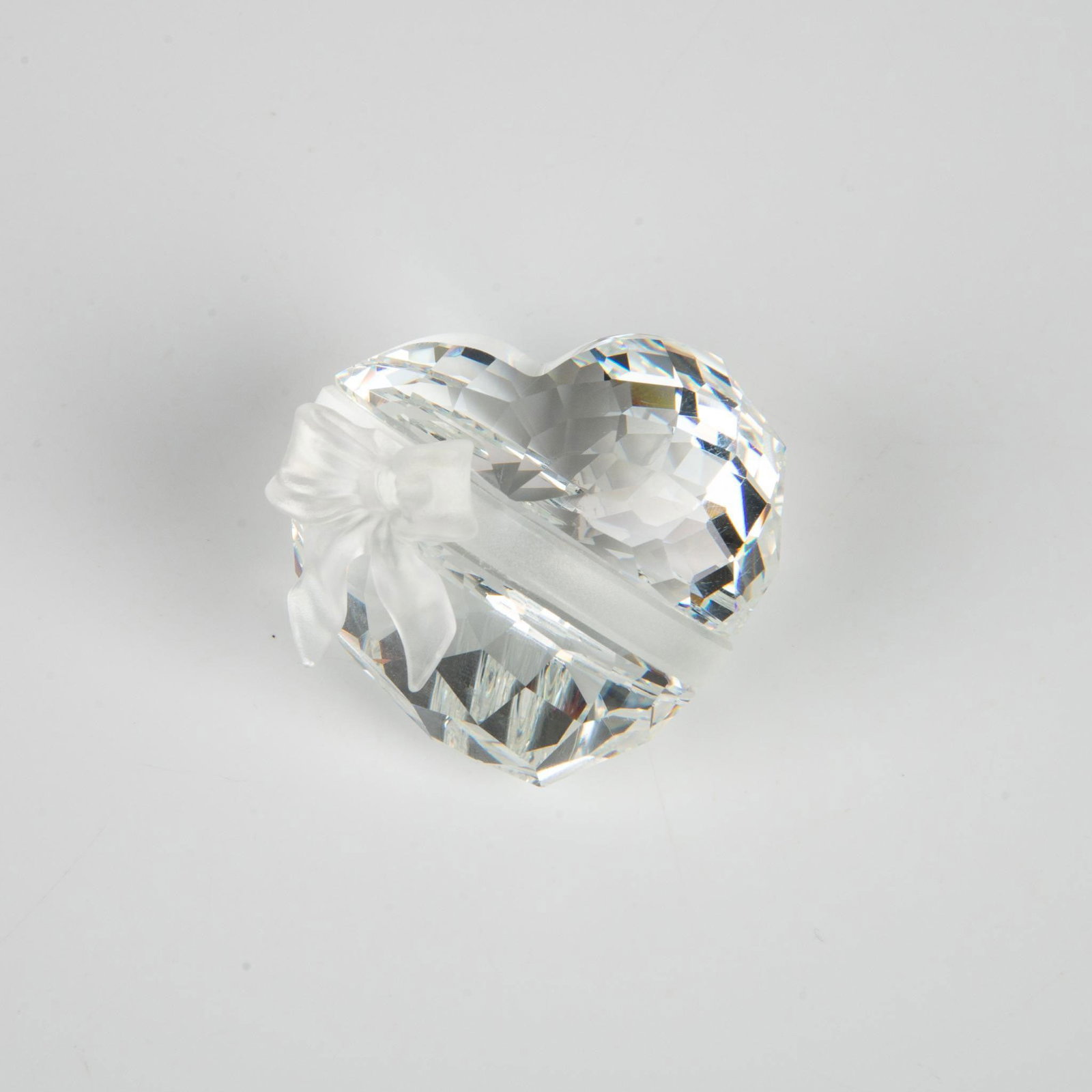 Swarovski Silver Crystal Figurine, Sweetheart 210035: A clear faceted figure of a round heart adorned with a matte ribbon. Part of the Exquisite Accents series. Swarovski marking. This item has its original box: 3.75"L x 3.75"W x 3"H. Artist: Edith Mair 