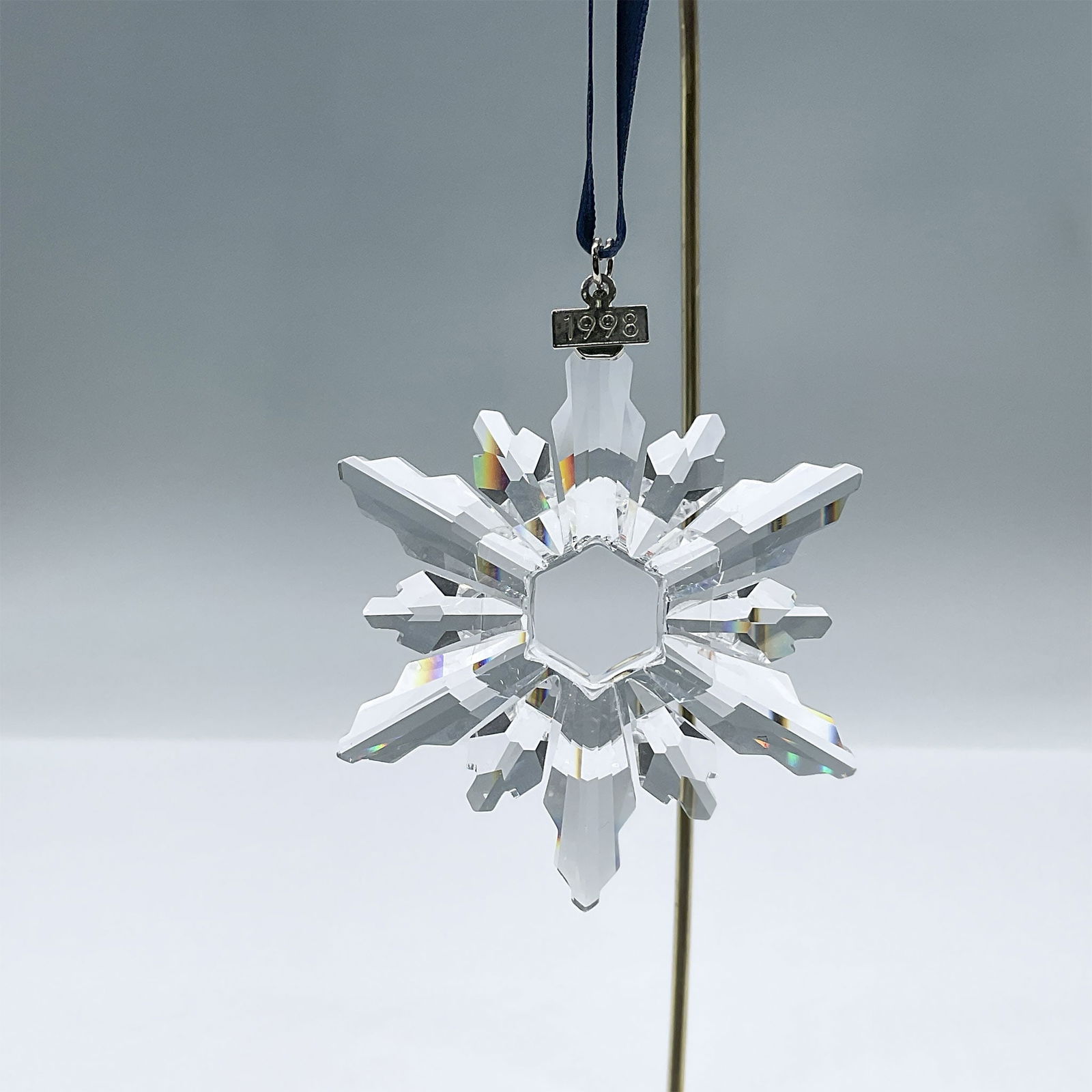 Swarovski Crystal Figurine, 1998 Christmas Ornament: This brilliant clear crystal ornament features 12 points, a metal tag with 1998 engraving, and a blue satin ribbon. Swarovski acid mark. 220037. Artist: Martin Zendron Issued: 1998 Dimensions: 2.75"W