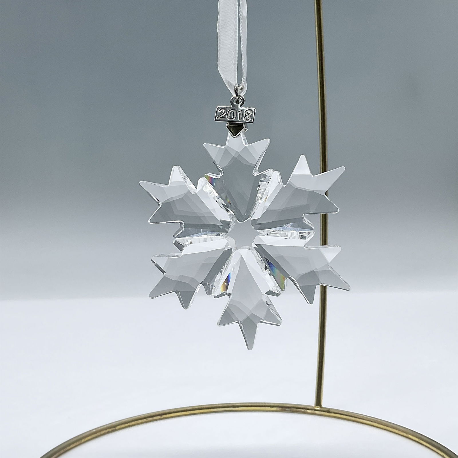 Swarovski Crystal Figurine, 2018 Christmas Ornament: This snowflake ornament features 156 clear crystal facets and a metal tag engraved with the year of issue on a white satin ribbon. Swarovski engraving. 5301575. Artist: Verena Castelein Issued: 2018 D