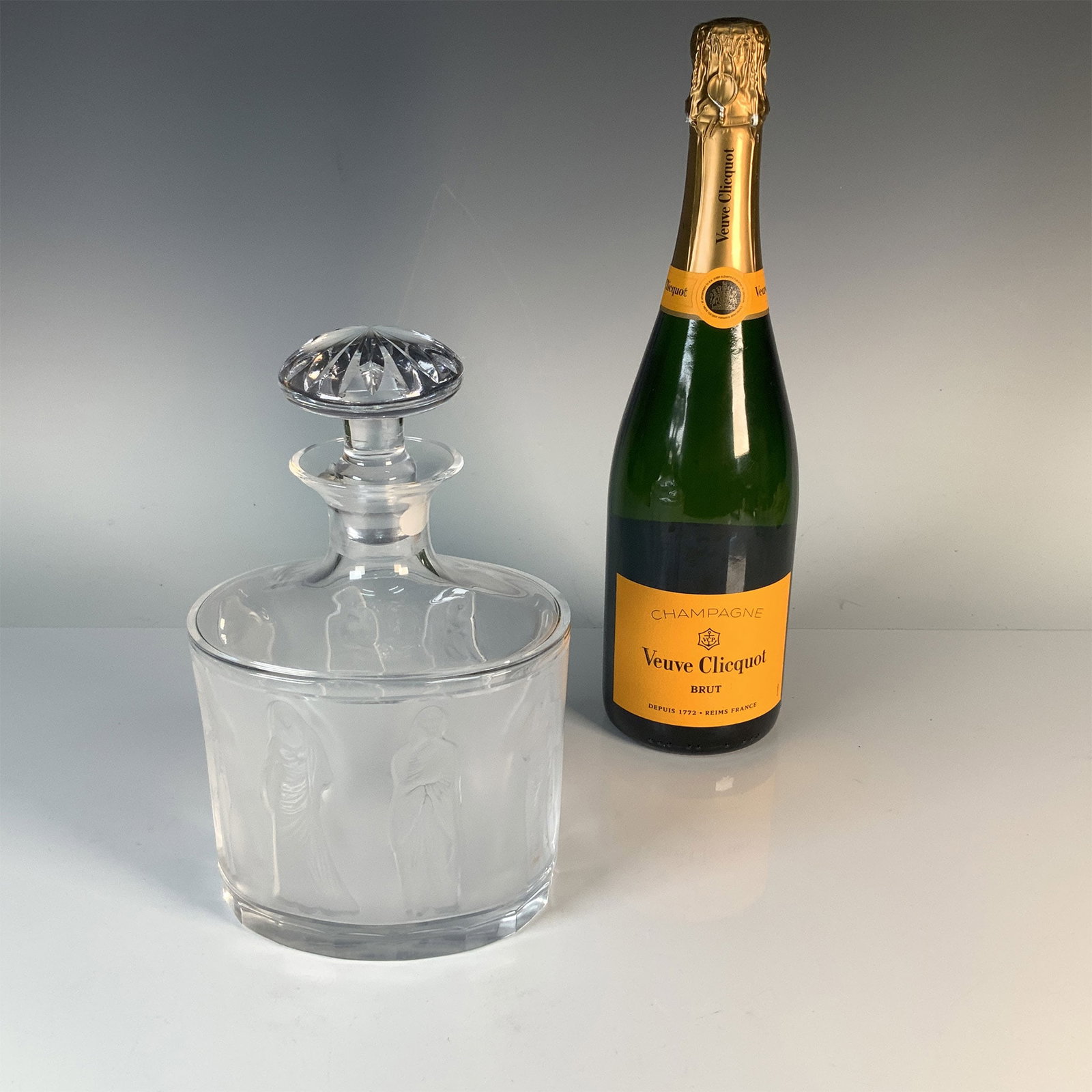 Lalique Femme Decanter with Stopper: This elegant Lalique "Femme" crystal decanter is a stunning representation of Ren? Lalique's iconic artistry. Standing 9 inches tall, the decanter features frosted draped female figures in graceful po