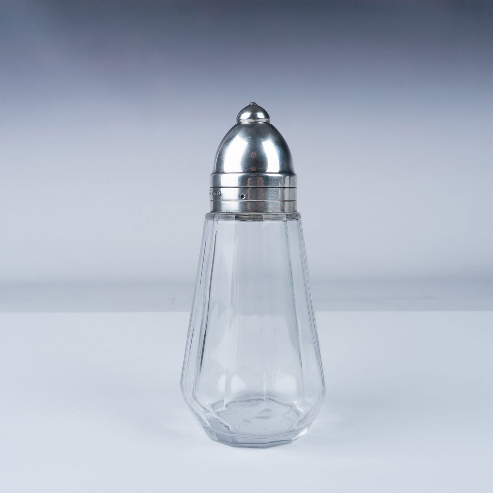 Christofle Silver-Plated and Glass Sugar Shaker: A sophisticated sugar shaker by Christofle, the renowned French silversmith celebrated for their exceptional craftsmanship and timeless designs. This elegant piece features a silver-plated cap and col