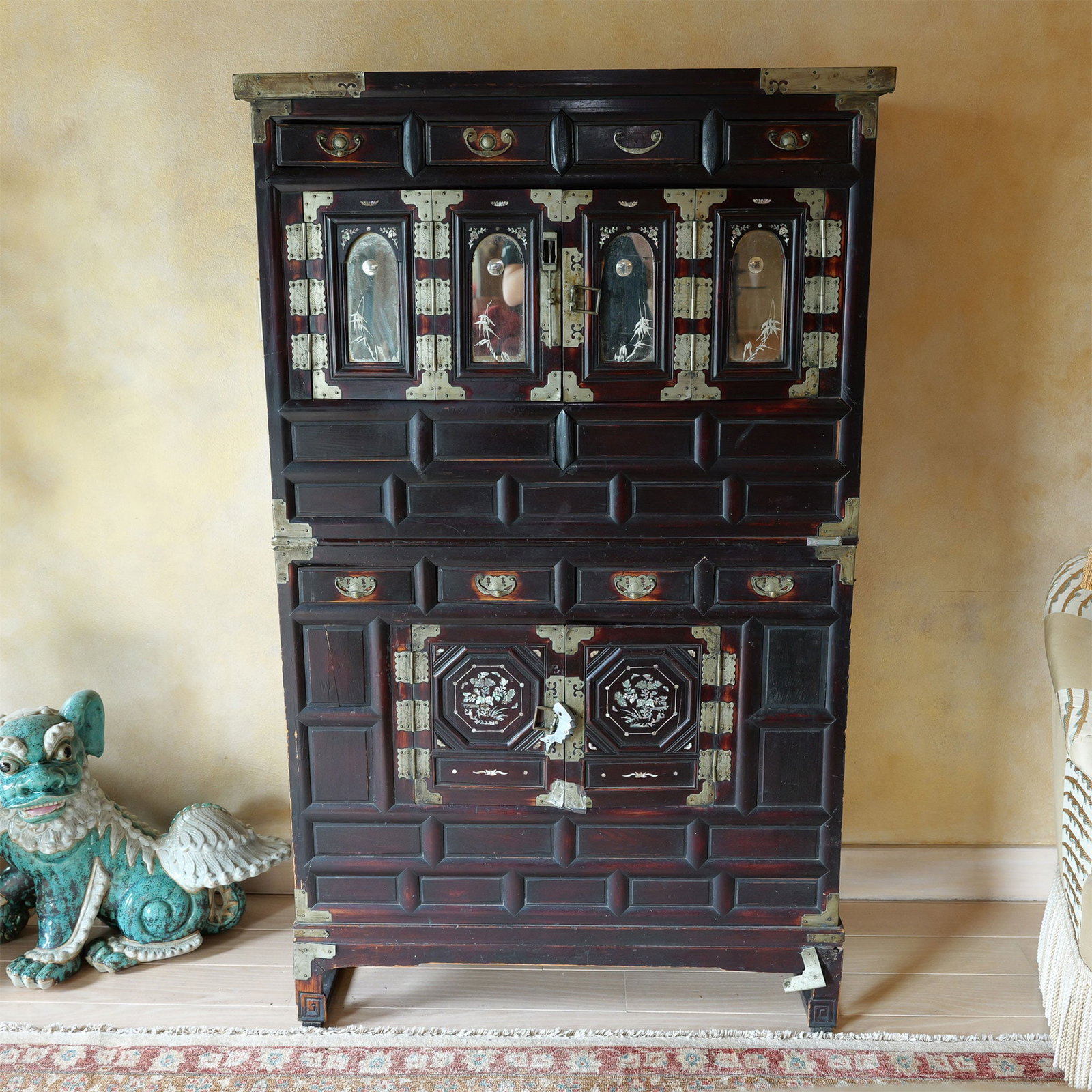 Korean Mother-of-Pearl Inlaid and Brass Two Part Cabinet: This exquisite lacquer cabinet showcases the elegance of traditional craftsmanship, featuring intricate mother-of-pearl inlay depicting floral and natural motifs. The piece is accented with ornate bra