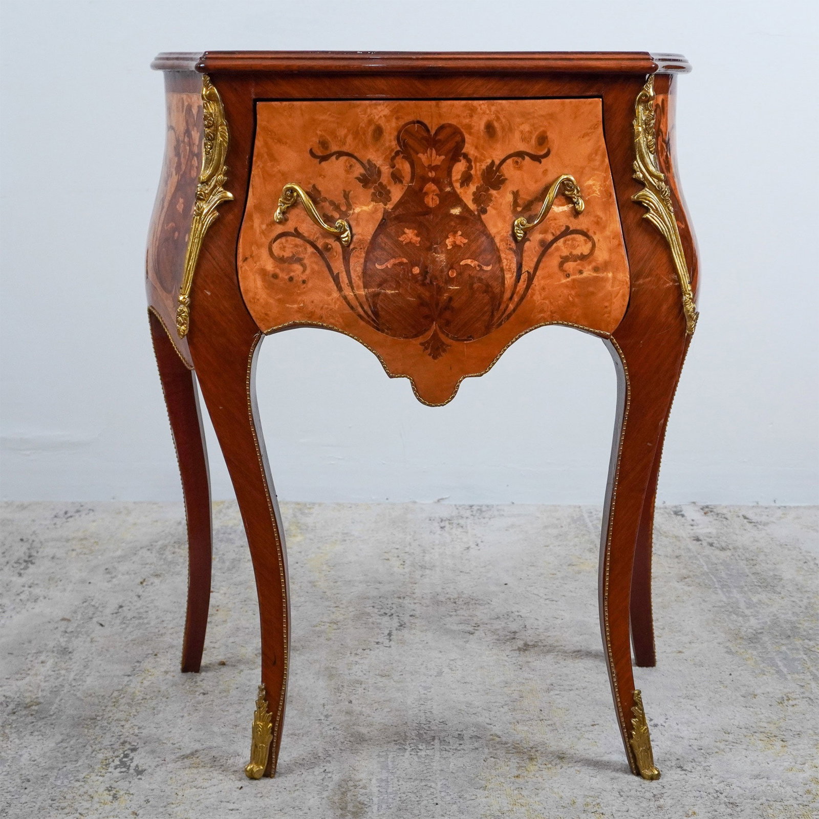 Louis XV-Style Inlaid Faux Marquetry Serpentine Side Table: A stunning Louis XV-style serpentine side table, featuring faux marquetry with floral and figural motifs. The table is adorned with gilded ormolu mounts along the edges, legs, and corners, enhancing i