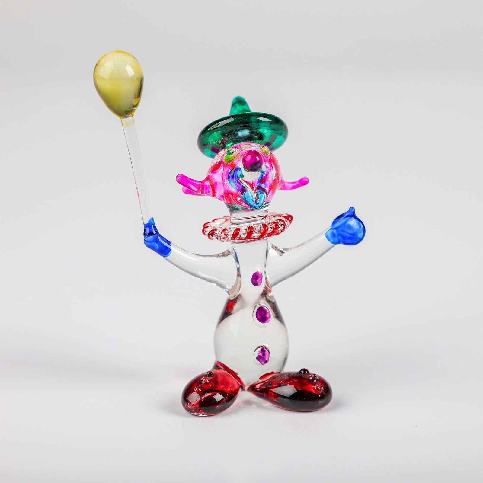 Glass Clown Figurine with Balloon: This charming glass clown figurine stands 3.5" tall and features vibrant colors and intricate detailing. The clown is crafted from clear glass, with highlights of red, blue, and pink throughout the fi