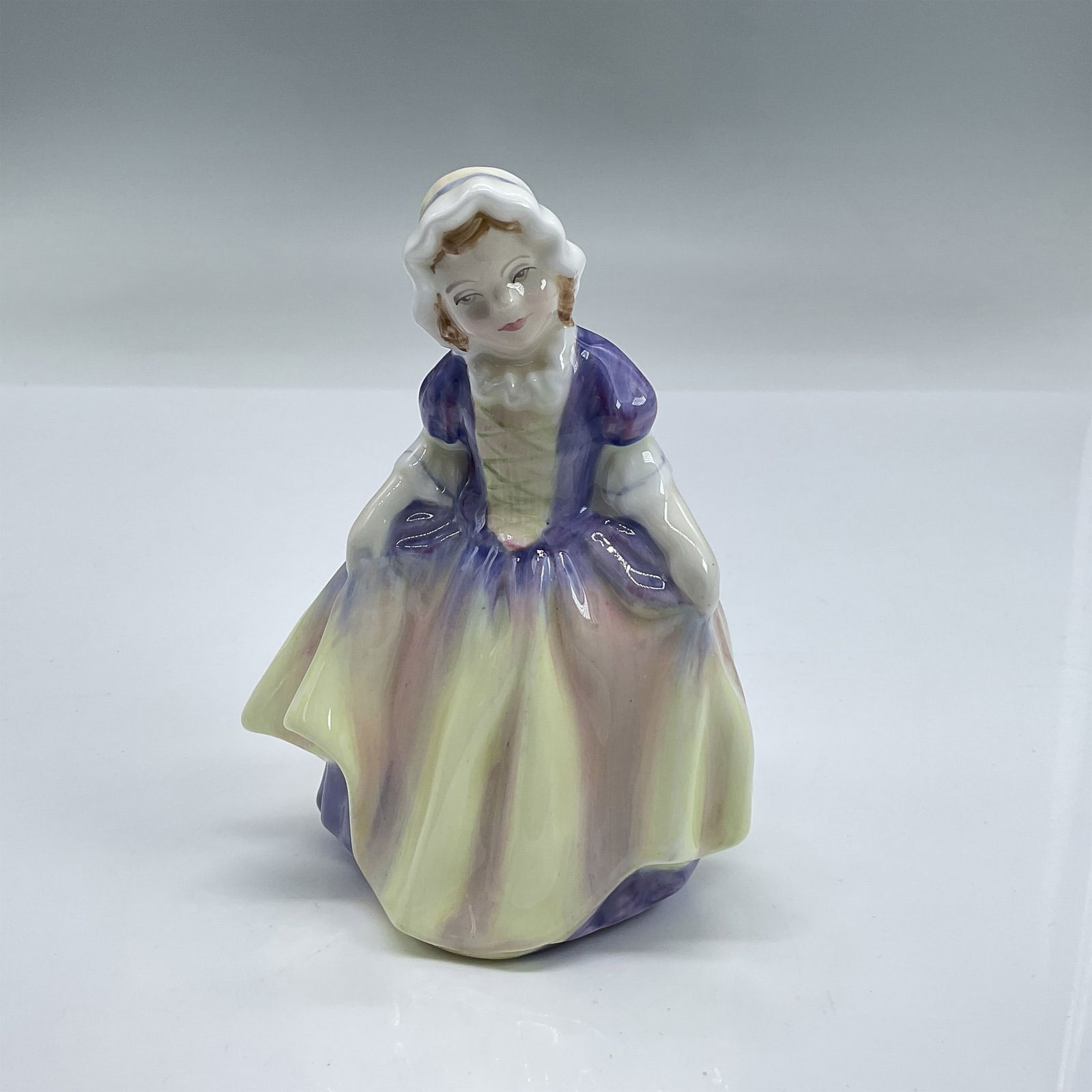 Dinky Do HN1678 - Royal Doulton Figurine: Glazed bone china figure of girl in a purple and yellow dress and white bonnet holding her skirt. Part of the Harradine Child Classics series. Royal Doulton backstamp. Dimensions: 3.5"L x 2.75"W x 4.5