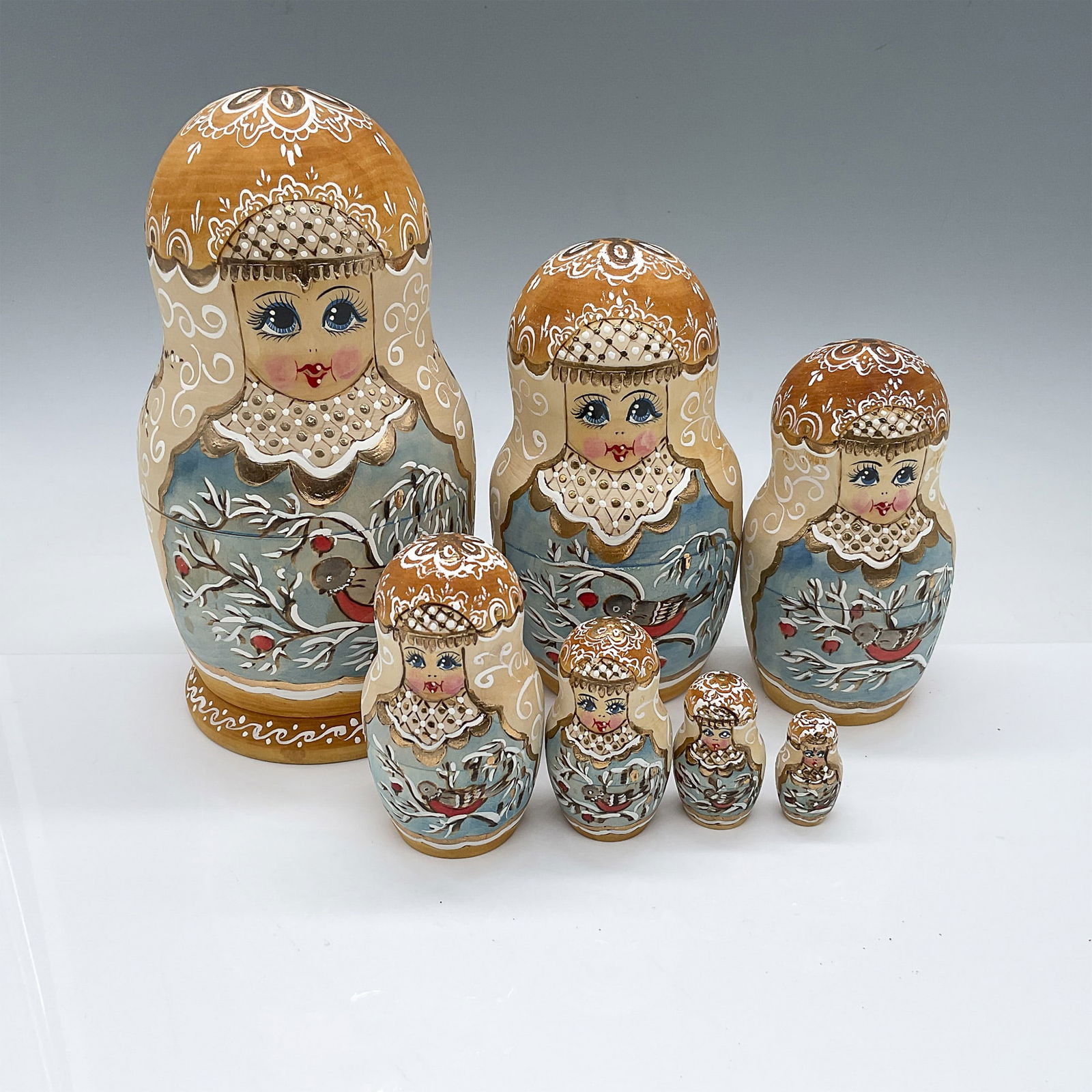 7pc in 1 Hand-Painted Russian Nesting Doll: A set of seven hand-painted Russian Matryoshka nesting dolls, adorned with intricate floral and bird designs enhanced by delicate gold accents and lace-like detailing. The largest doll measures 7.5"H,