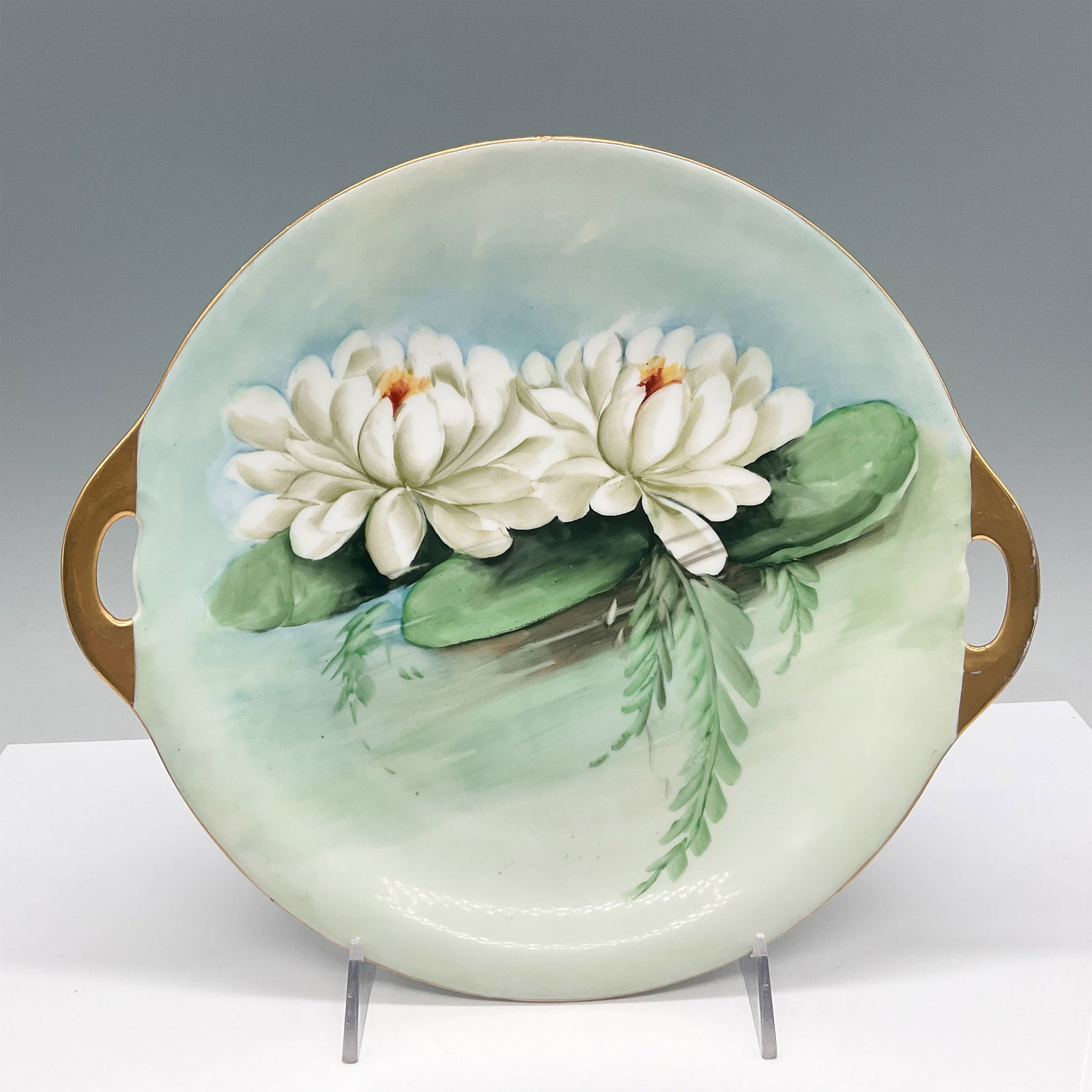 Hutschenreuther Hand-Painted Cake Plate with Water Lily: A beautifully hand-painted porcelain cake plate featuring a serene water lily design in soft shades of green and white, accented with touches of gold around the handles. The piece showcases exquisite